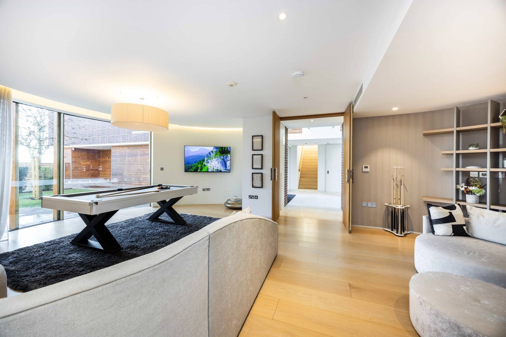 Entrance transition looking past a white pool table room into a curved hallway with oak floors, Love Locations WD7.
