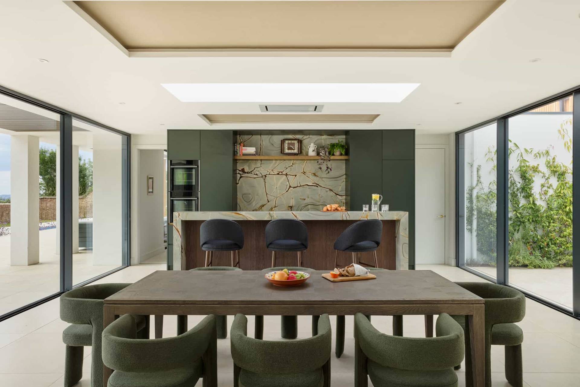 Modern open-plan kitchen and dining layout showcasing dramatic green marble splashback and skylight illumination, ideal for food editorial filming, Love Locations.