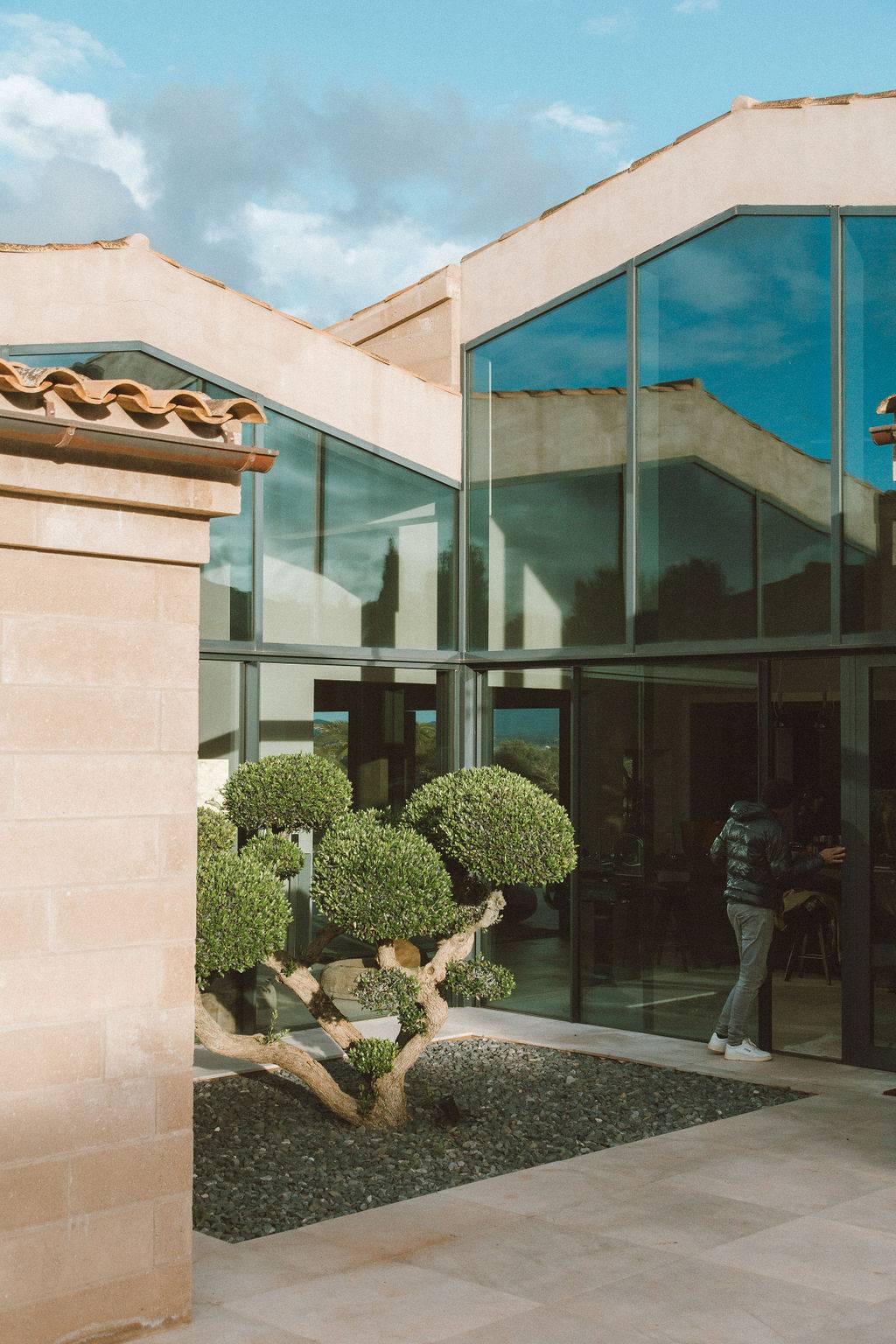 Modern glass-walled villa building surrounded by manicured topiary trees and gravel paths, Love Locations 07630.