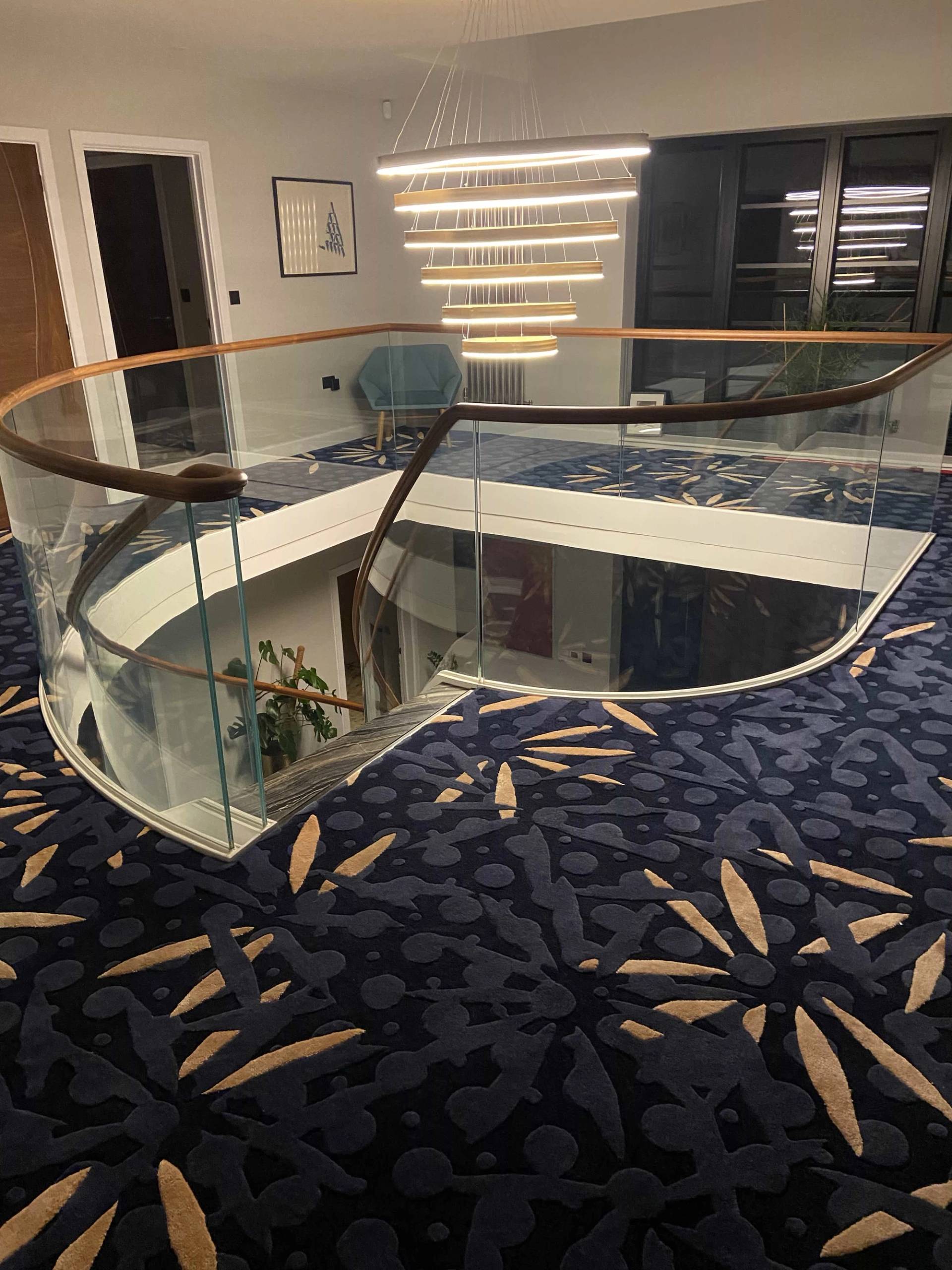 Upper floor galleried walkway featuring patterned dark carpets and glass balcony balustrades, Love Locations CB2.
