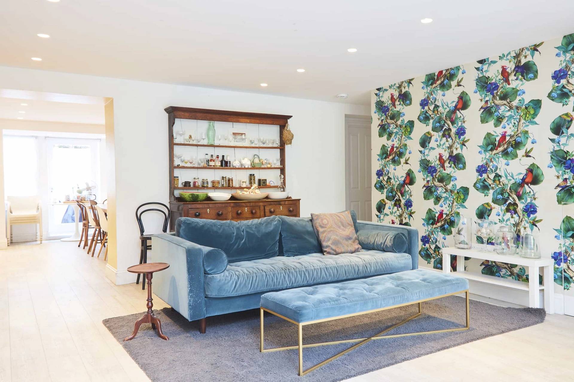 Victorian reception room featuring a plush blue velvet sofa, matching ottoman, floral wallpaper, and open fireplace, Love Locations N5.