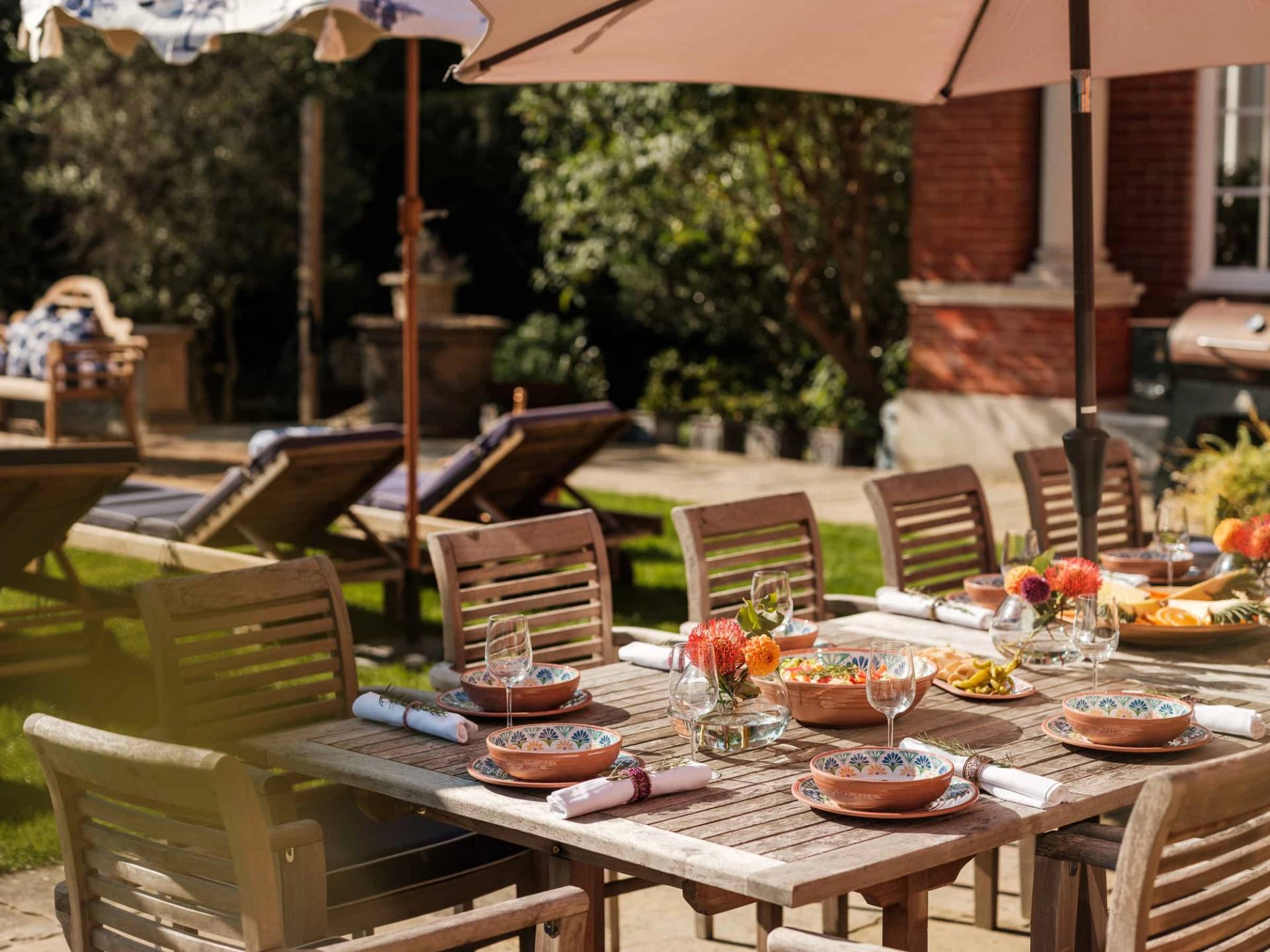 Al fresco summer dining setup featuring rustic wooden table, chairs, parasols, and garden views, Love Locations RG42.