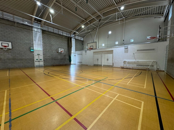 Love Locations multi-use indoor court space Cockfosters: Clean physical education hall with clear overhead lighting trusses, optimized for music videos and team sports filming.