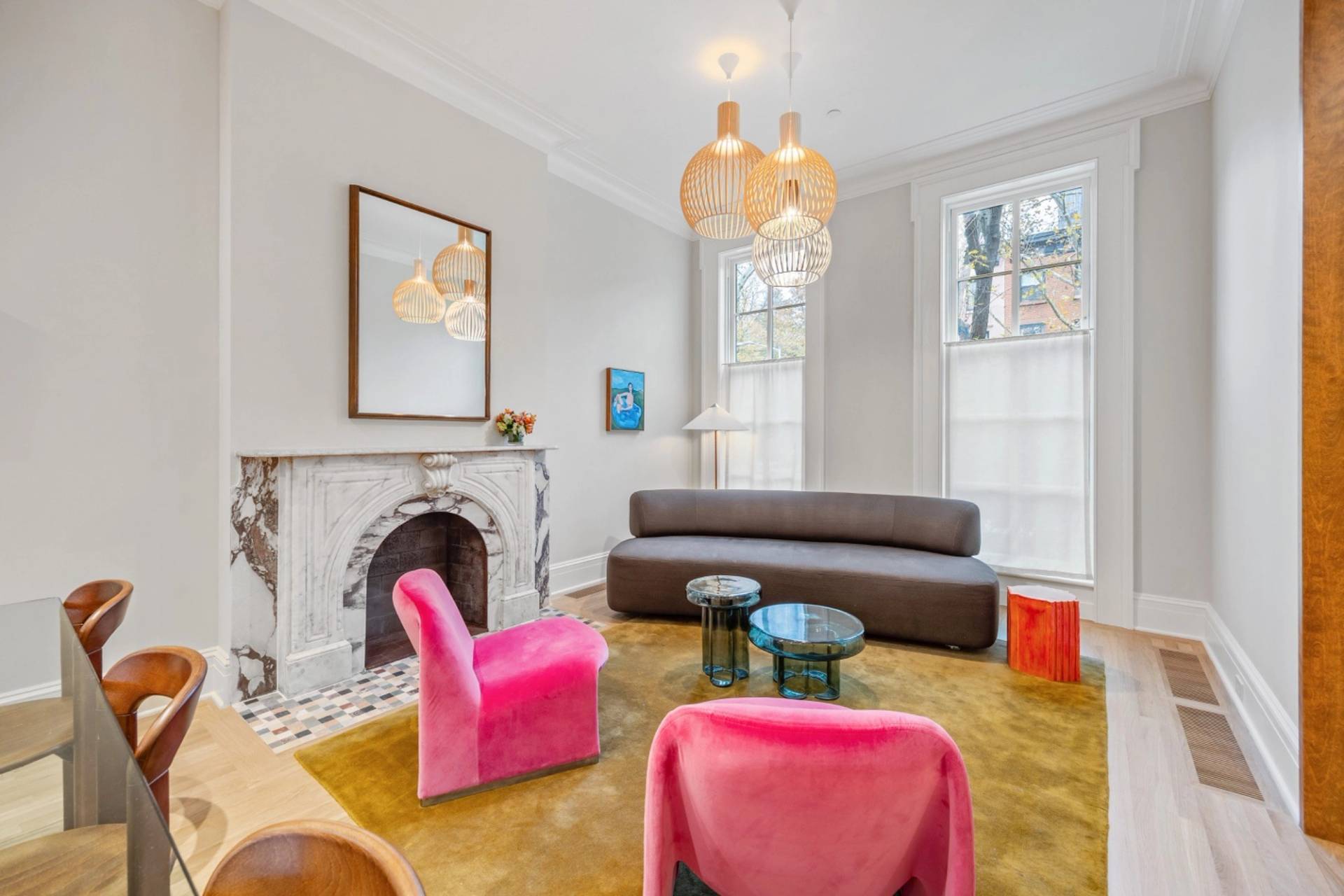 Bright formal living room photoshoot space in Boerum Hill Brooklyn through Love Locations, showcasing dual hot pink velvet armchairs, a curved grey sofa, a marble fireplace, and tall sash windows.