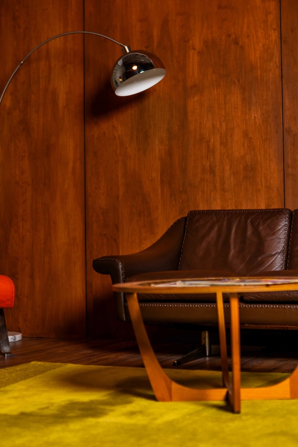 Close-up shot of a mid-century dark leather couch set against warm timber wall panelling in a North London studio, Love Locations N15.