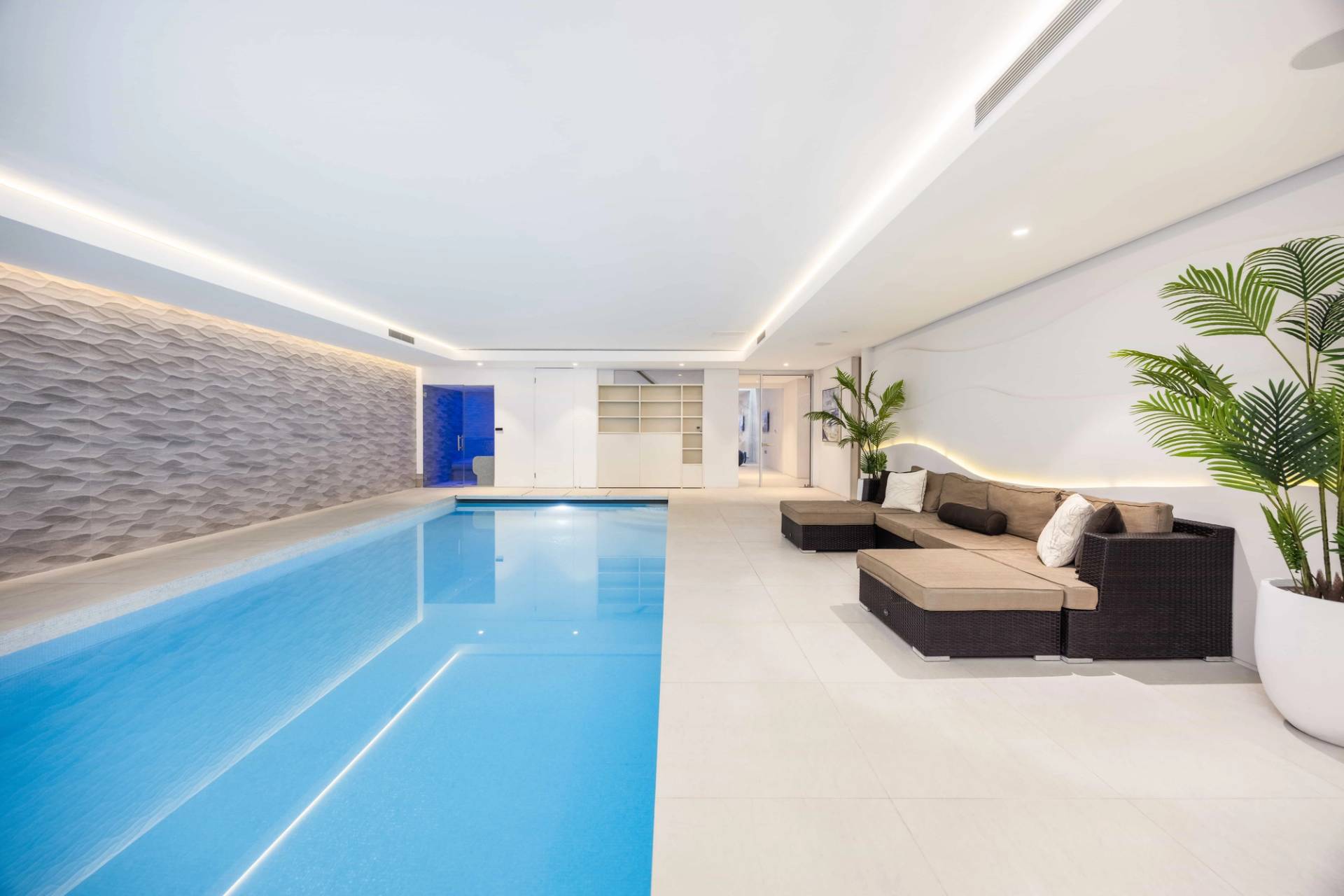 Indoor swimming pool hall featuring cream lounge sofas set against a textured stone feature wall, Love Locations WD7.