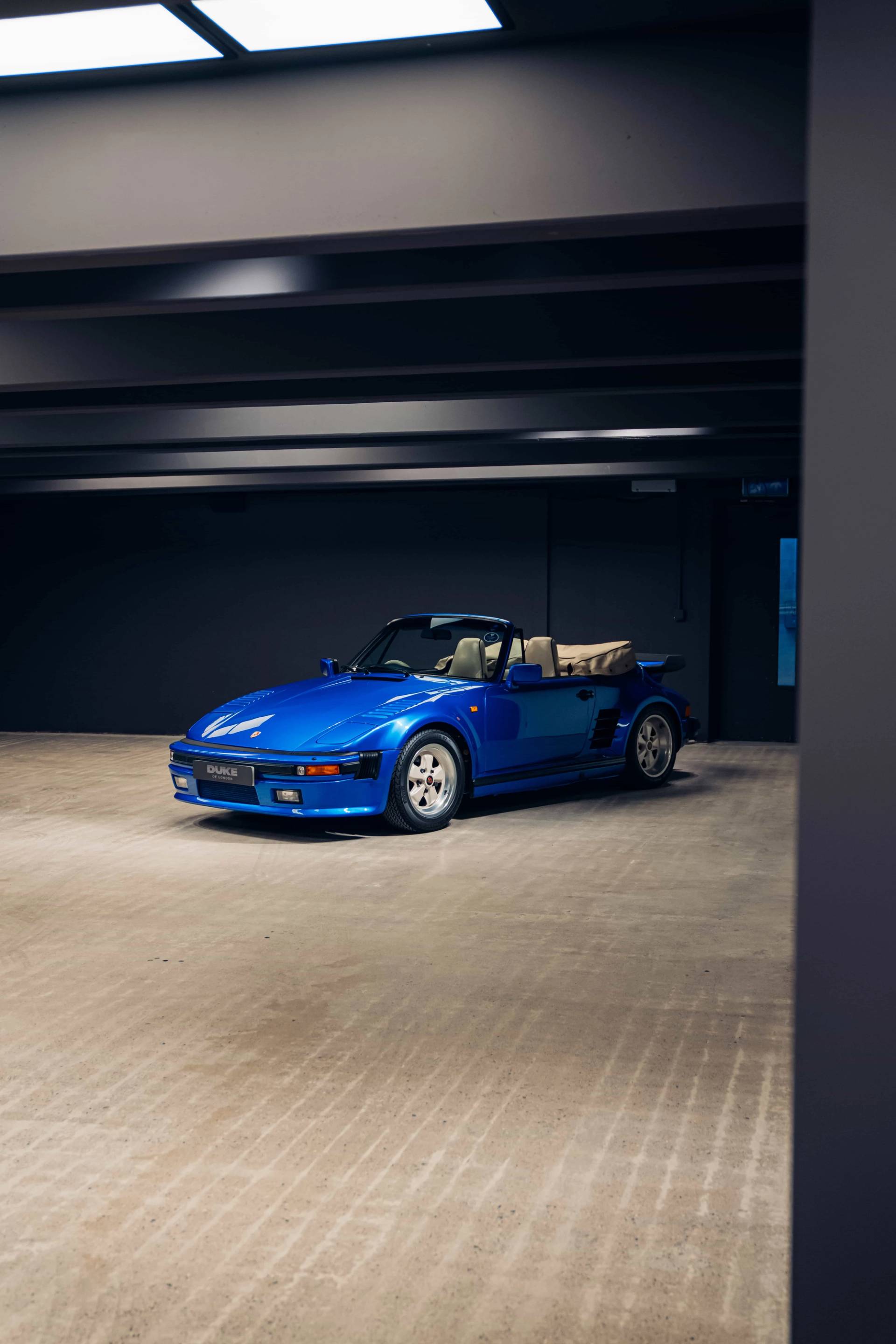 Classic blue sports car parked against dark concrete walls in a subterranean production space by Love Locations.