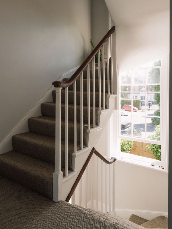Staircase view looking past a large sash window flooding natural daylight onto carpeted steps, Love Locations SW9.