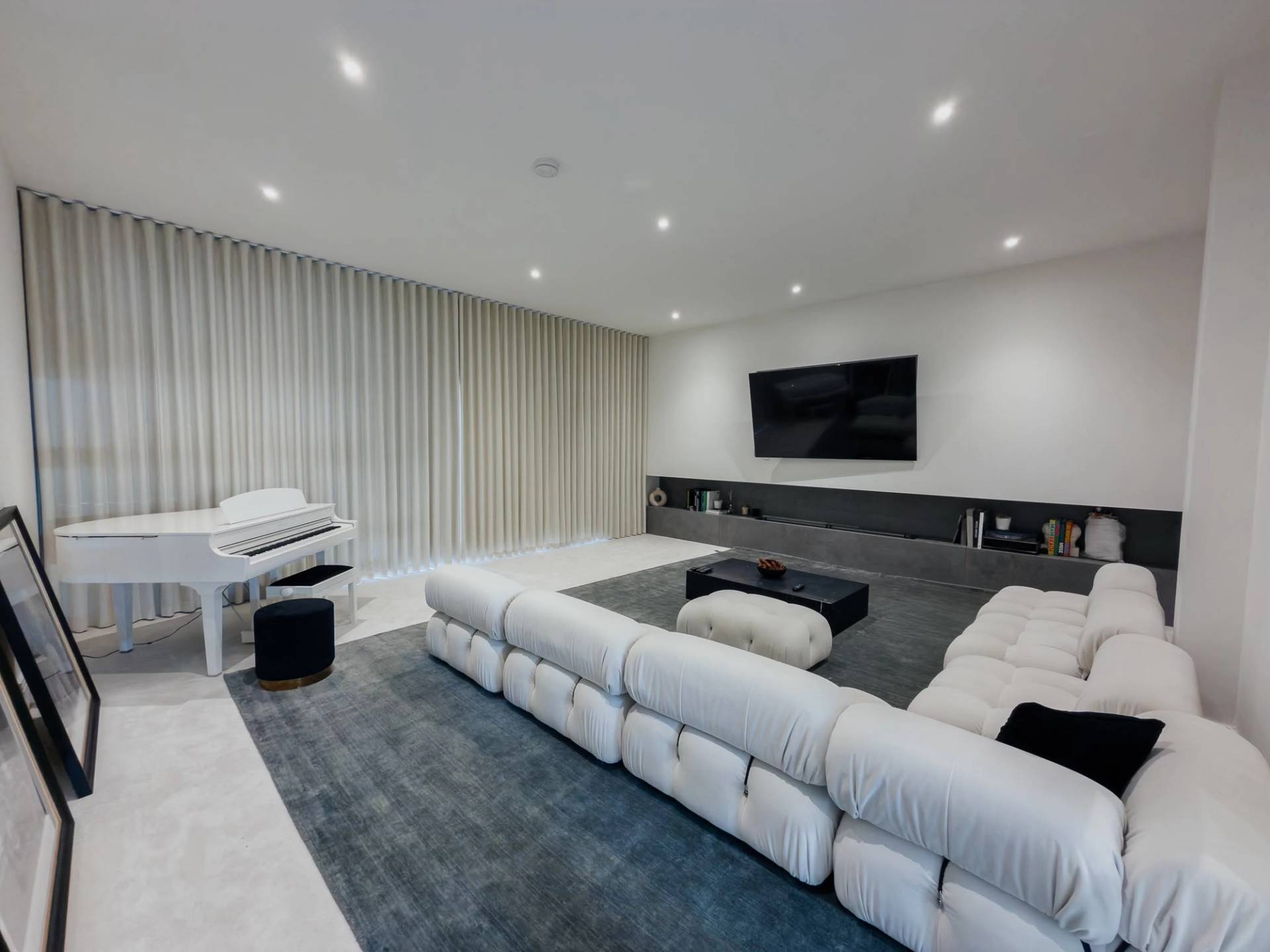 Broad view of a modern open-plan lounge film location in Barnet EN4 from Love Locations, featuring a plush cream modular sofa, white grand piano, and floor-to-ceiling window drapes.