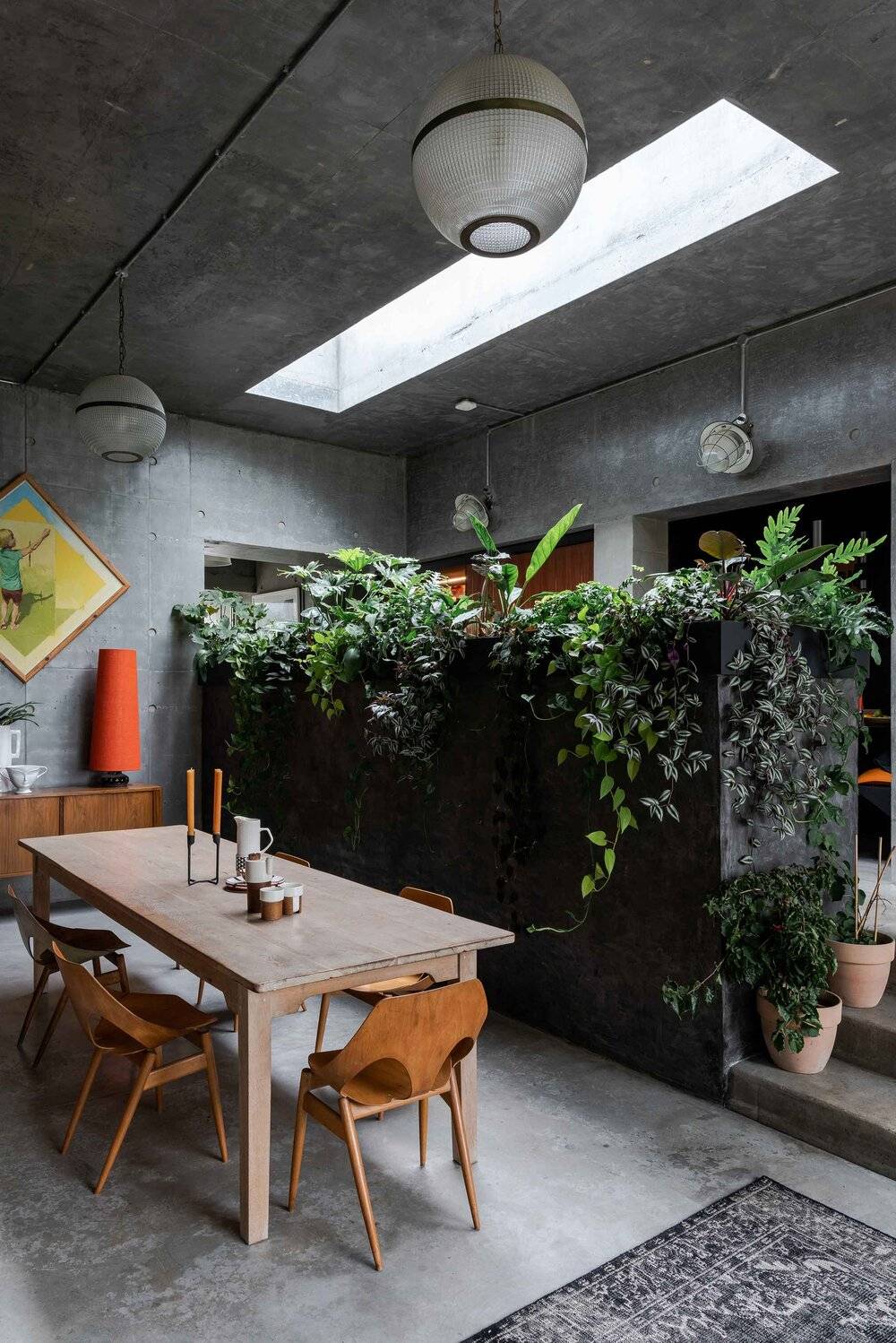 Brutalists concrete dining space in BN7 with lush overhead planter wall, wooden dining table, skylight, and polished concrete floors, Love Locations Plumpton Green.