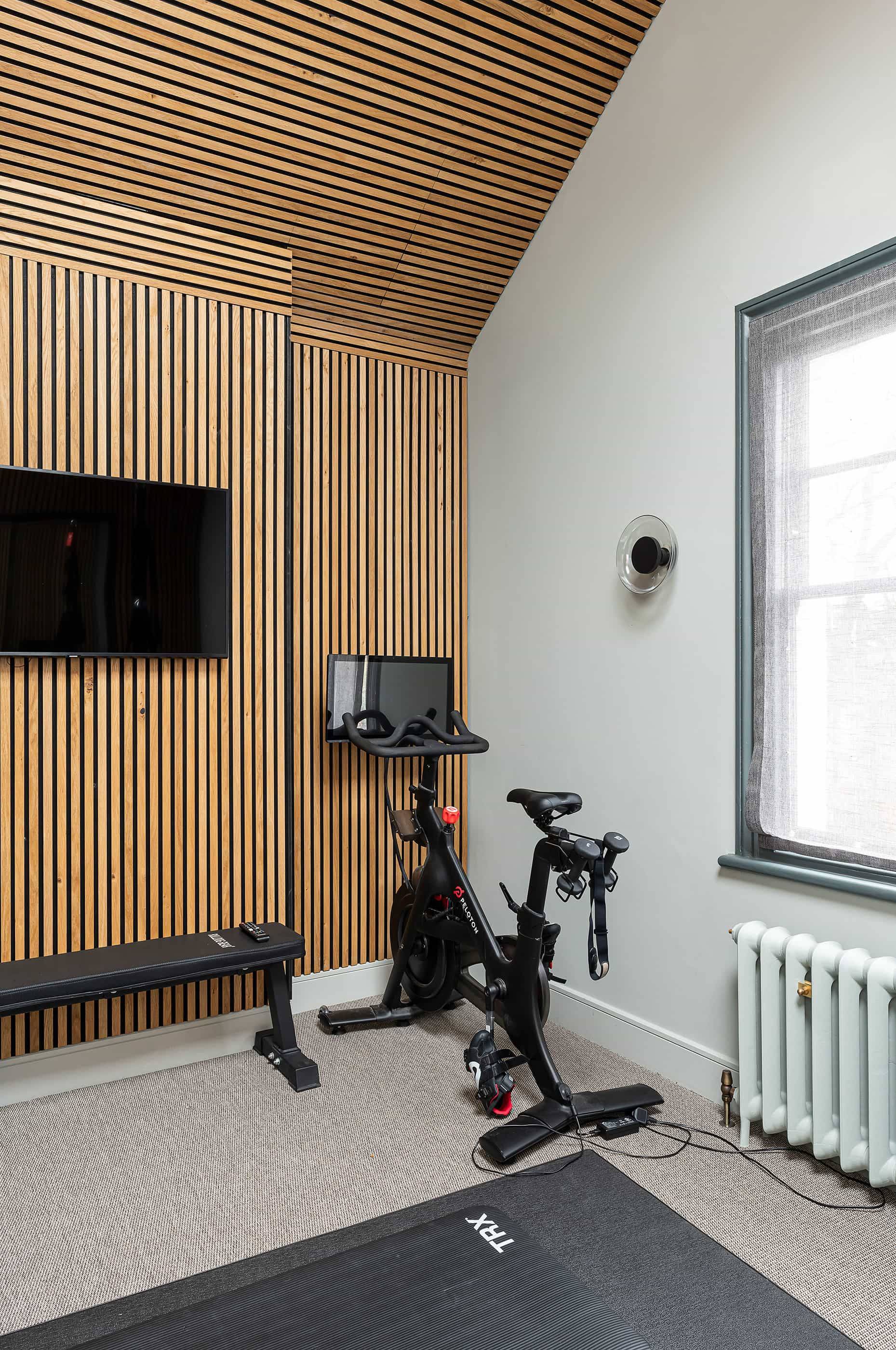 Modern home workout room featuring slatted timber wall cladding, Peloton stationary bike, and workout bench, Love Locations NW6.