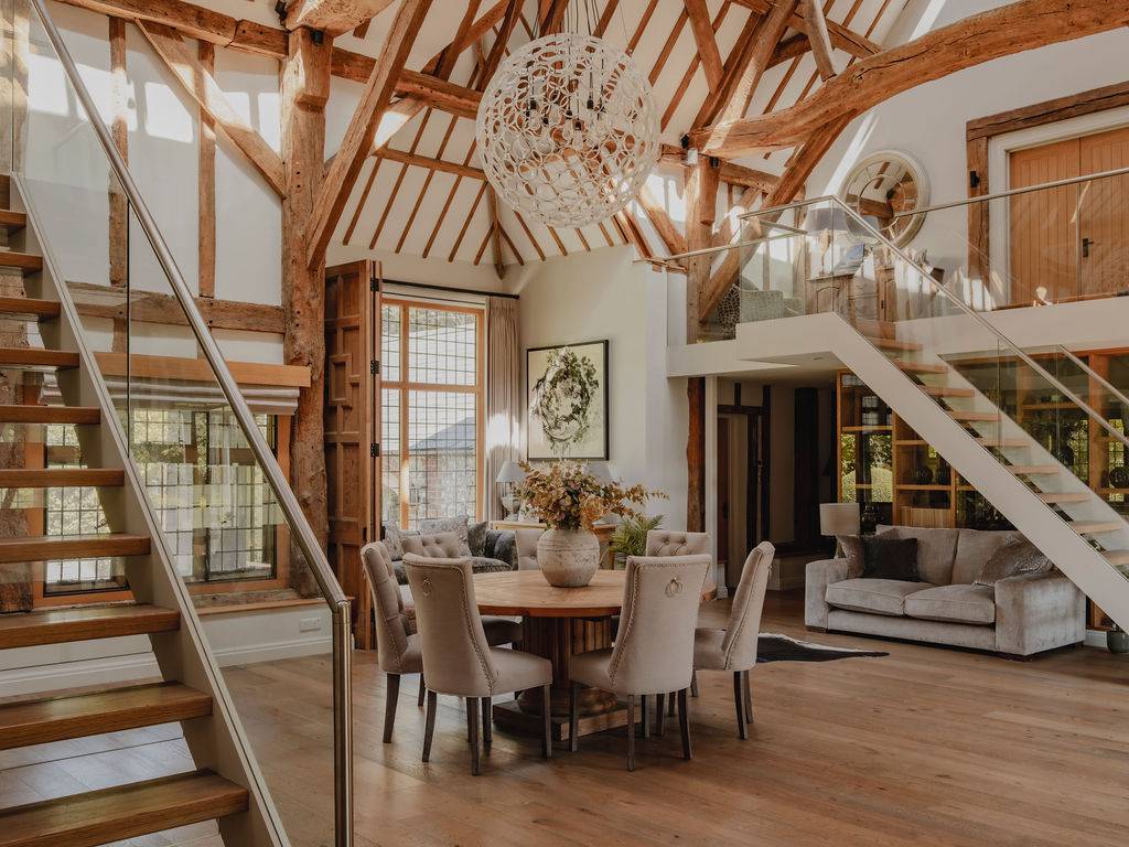 Wide shot of a grand open-plan barn room featuring a round central dining table beneath an intricate orb chandelier, Love Locations.