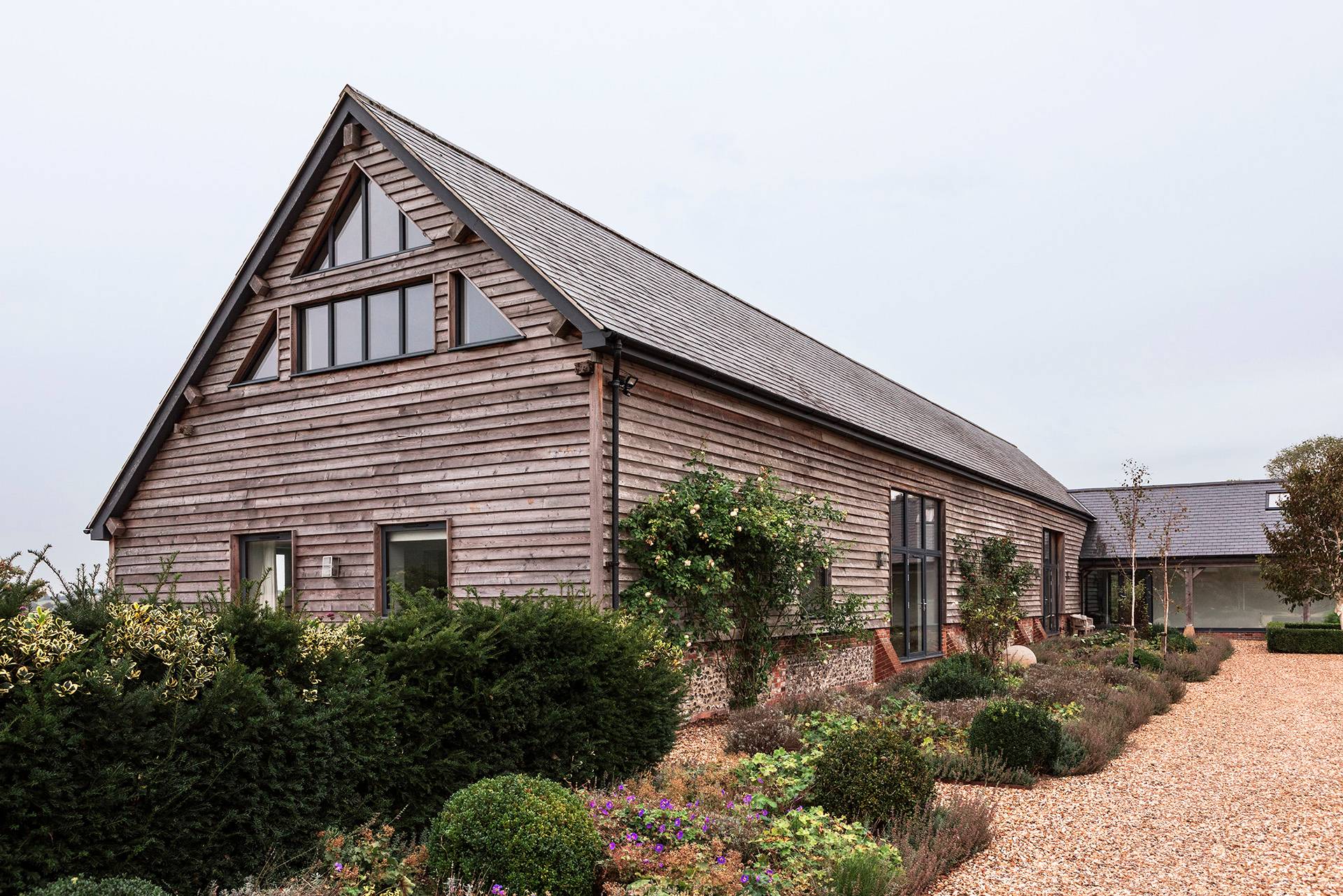 Timber-clad converted barn rear facade set behind landscaped garden borders and gravel paths, Love Locations SN8.