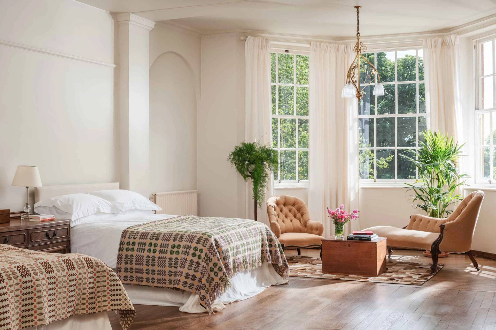 Bright master bedroom shoot location through Love Locations, displaying tall multi-pane windows, light neutral walls, and comfortable seating.