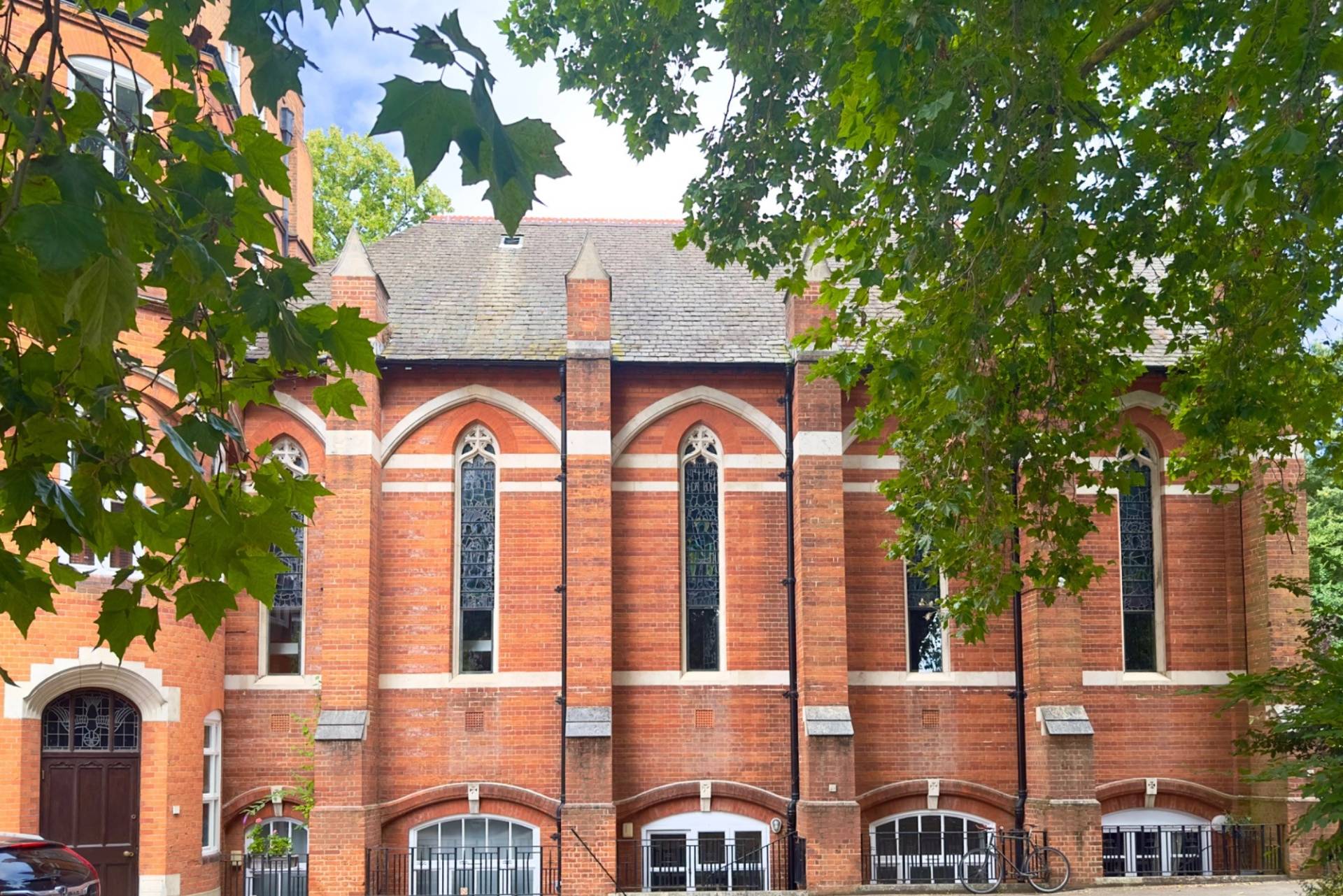 Red brick exterior facade of a period Victorian chapel film location in Oval SE5 through Love Locations, showing tall lancet windows and lush tree coverage.