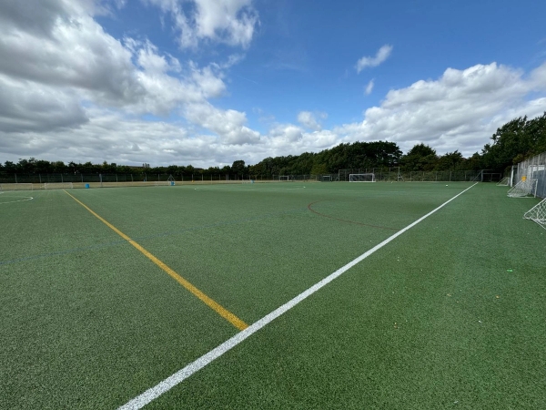 Love Locations synthetic turf field location EN4: Wide tracking perspective across a 3G astro-turf sports ground under an open sky, excellent for athletic training scenes and sports filming.