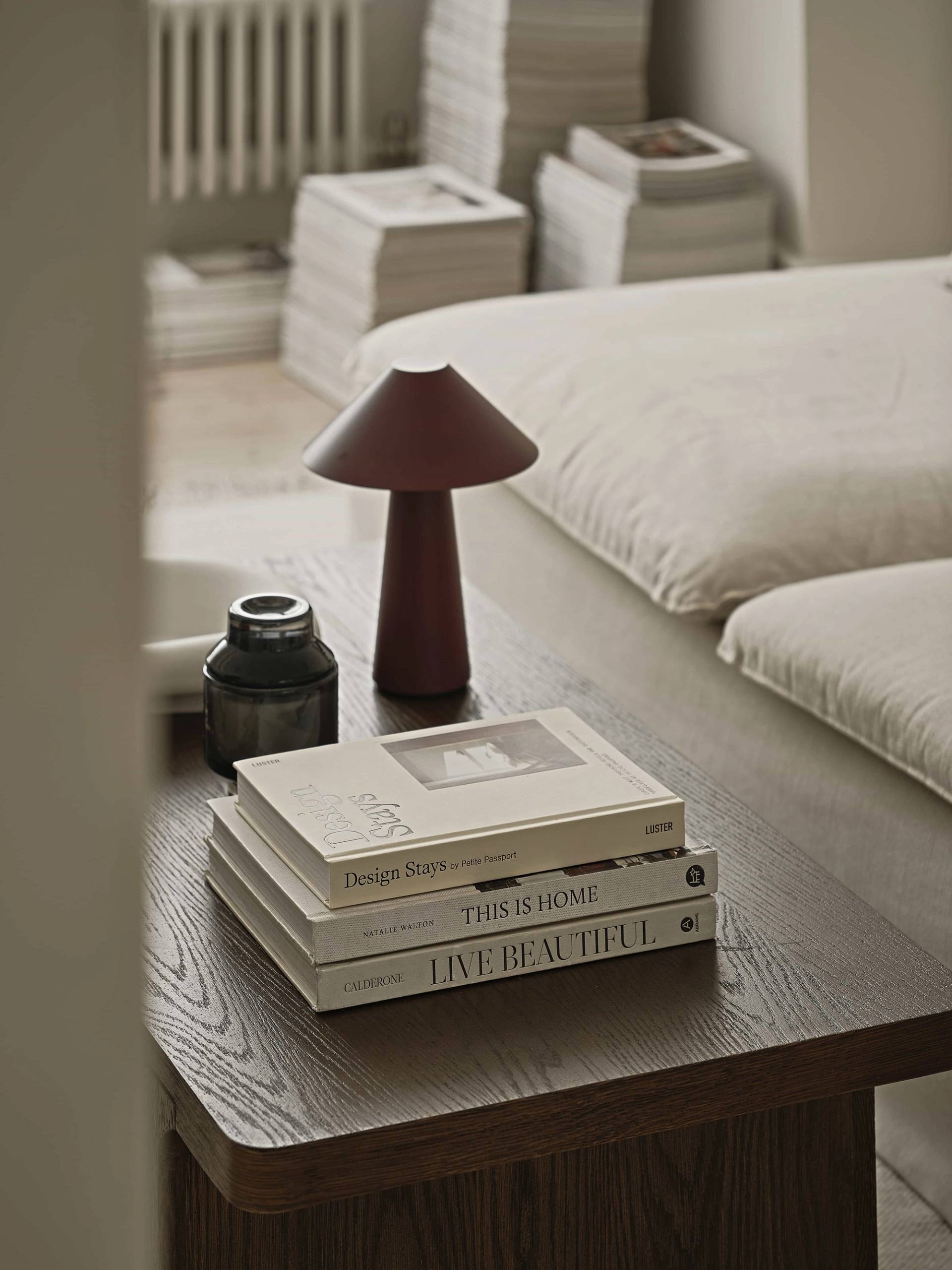 Detail shot of a dark timber coffee table styled with art books and a burgundy mushroom table lamp, Love Locations E4.