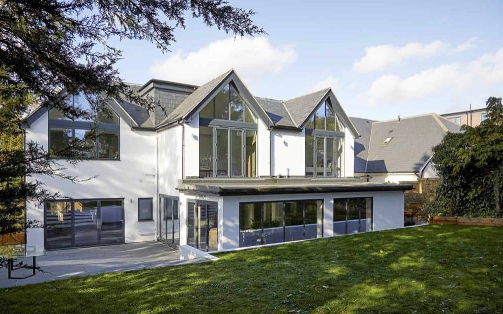 Modern white gabled mansion rear garden elevation hero cover image in Loughton, IG10 featuring floor-to-ceiling glass sliding doors, manicured green lawns, and private sun terraces, the ultimate high-visibility backdrop for feature film productions, TV drama filming, luxury brand commercials, and high-fashion editorials via Love Locations.