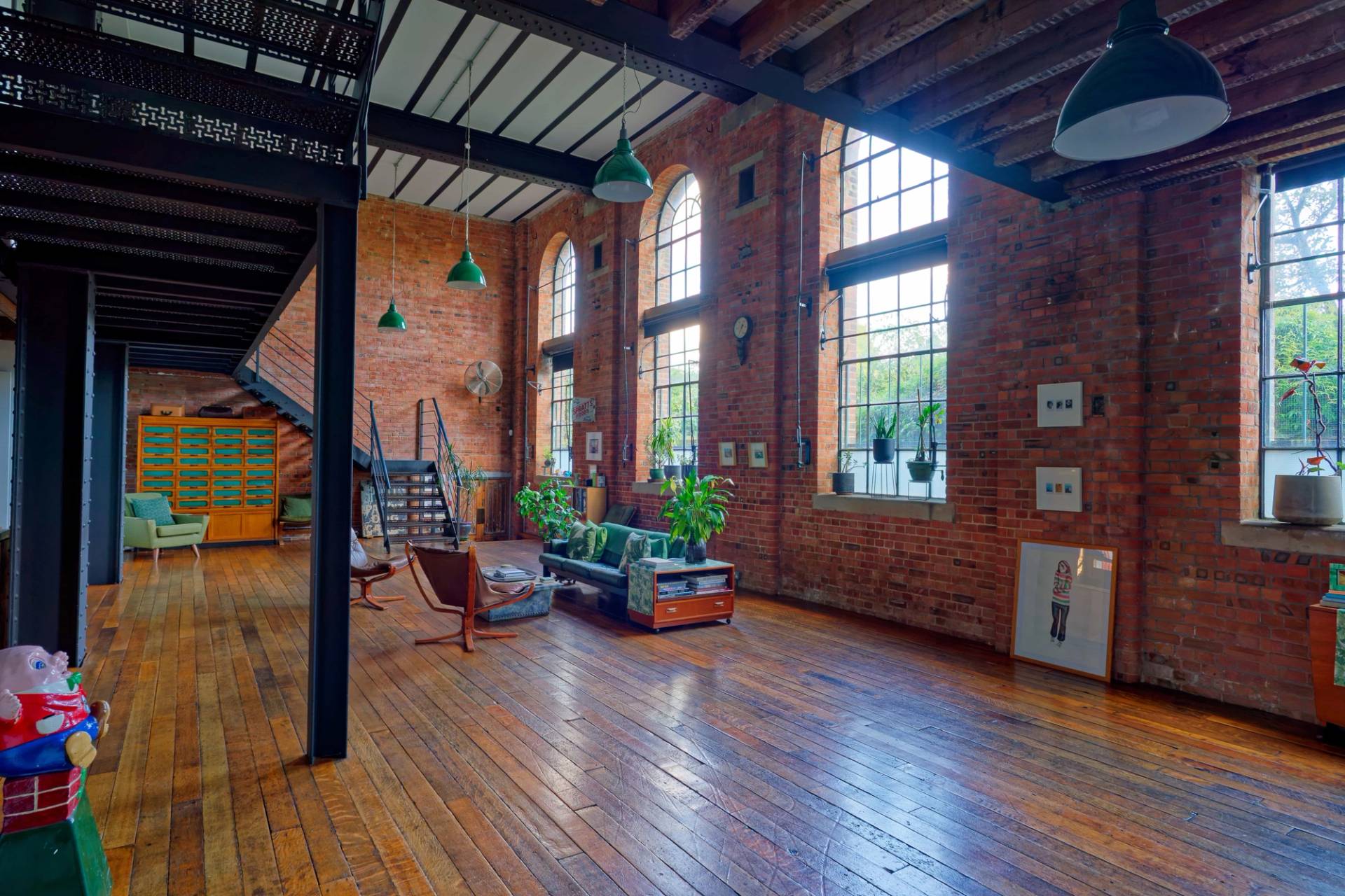 Industrial reception room with double-height arched warehouse windows, exposed red brickwork, and green pendant lights in E14, Love Locations.