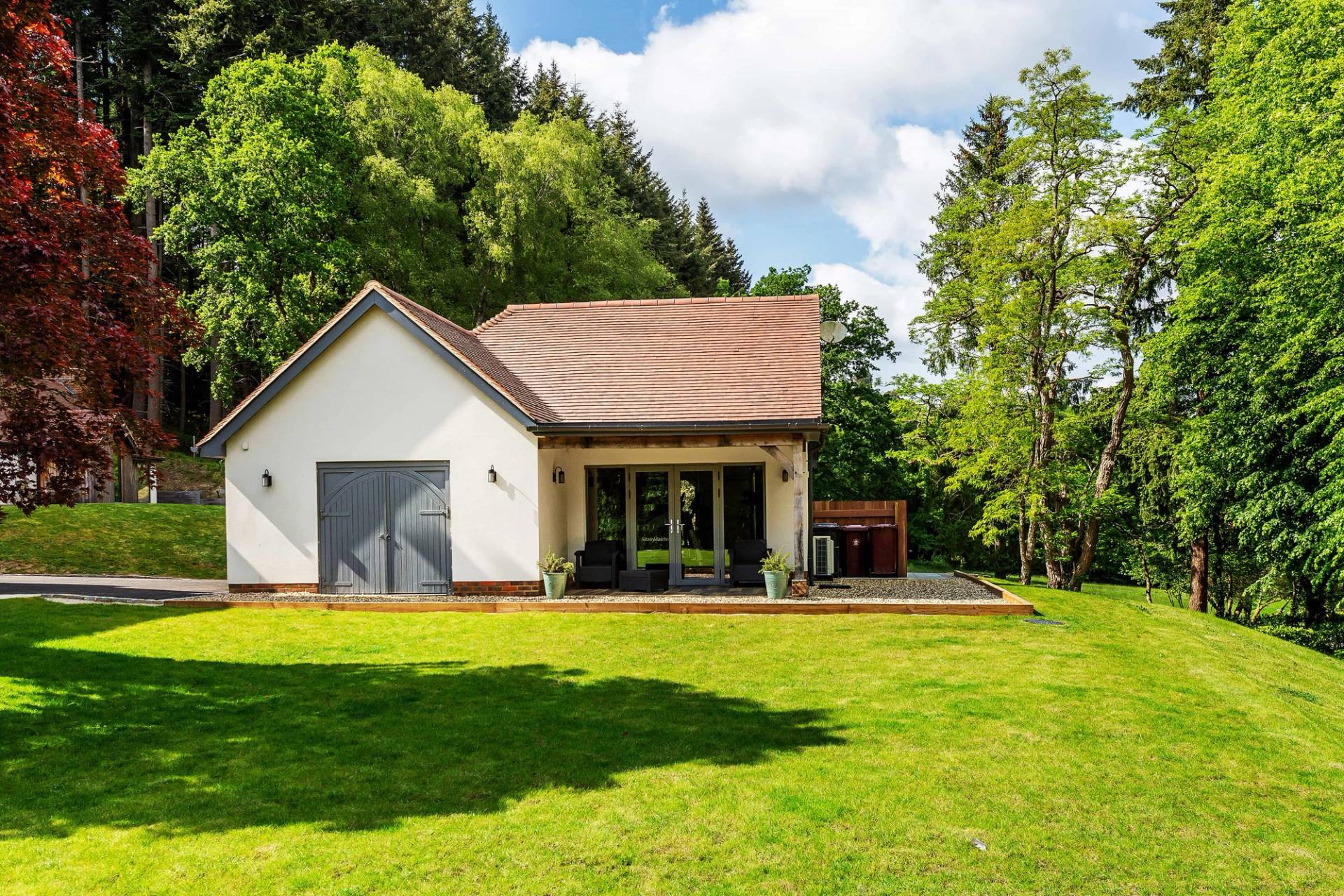 Detached timber-clad pool house or garden lodge with a manicured lawn, perfect for outdoor lifestyle shoots, Love Locations.