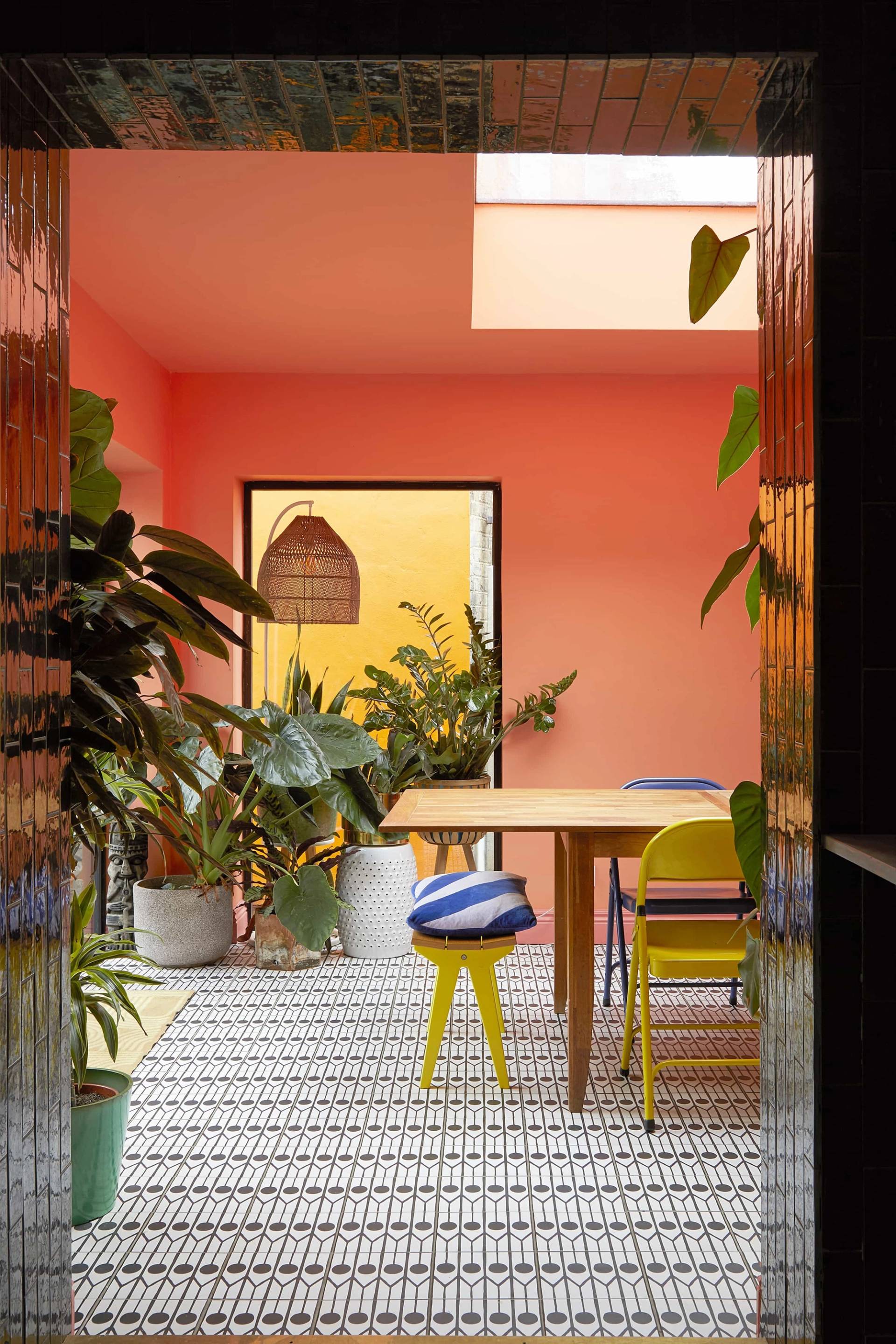 Bright coral orange dining extension featuring a large wooden dining table, yellow chairs, and geometric floor tiles, Love Locations SE6.