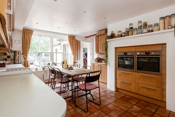 Broad perspective of a rustic kitchen and breakfast room with clay tiled flooring and wide windows looking out to the estate grounds from Love Locations.