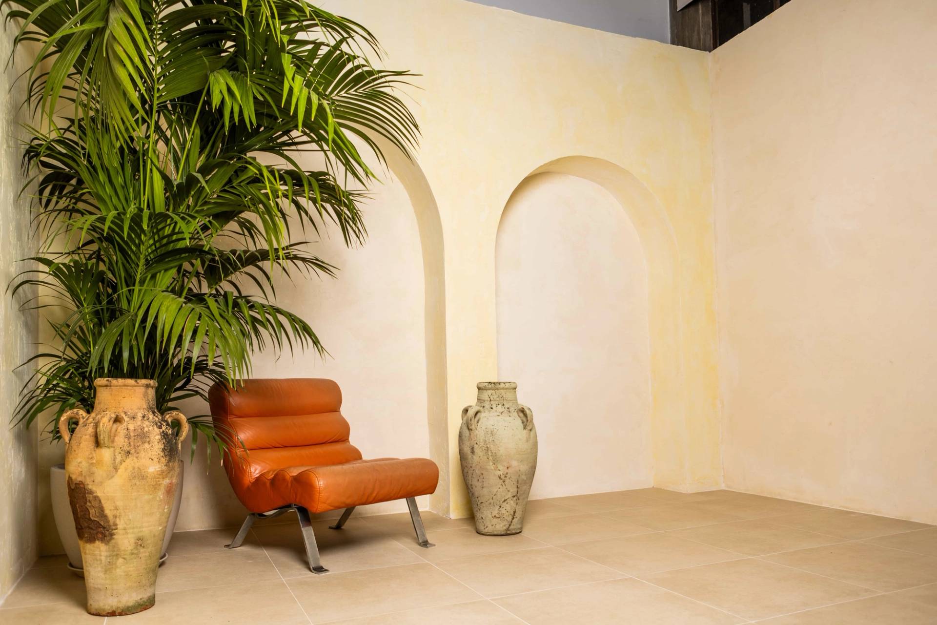 Plaster arch backdrop set with tropical potted palm, rustic urn, and orange leather armchair in a North London studio, Love Locations N15.