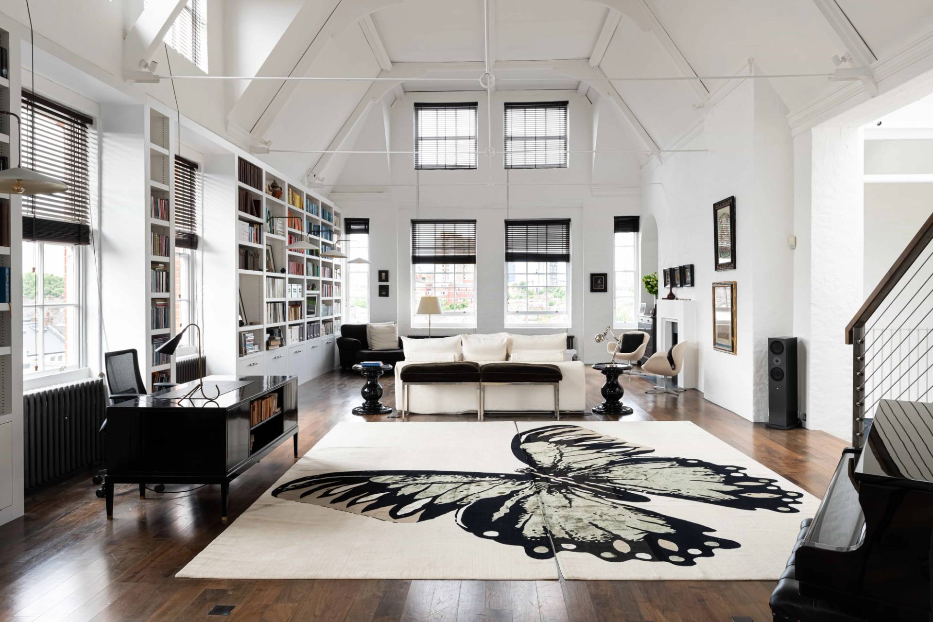Grand double-height vaulted loft bedroom with white A-frame ceiling beams, butterfly pattern rug, and floor-to-ceiling bookshelves in Battersea, Love Locations SW11.