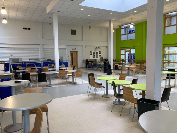 Love Locations contemporary school canteen Chelmsford Essex: Light-flooded dining hub with modern round tables and green chairs under a bright skylight architectural ceiling, perfect for youth-targeted brand campaigns.