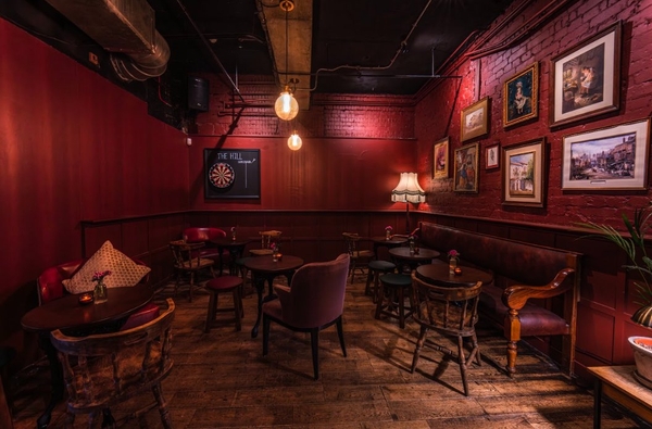 Moody, red-lit speak-easy style lounge corner featuring dark wood panelled walls, vintage framed artwork, and intimate seating, perfect for cinematic film sets, Love Locations.