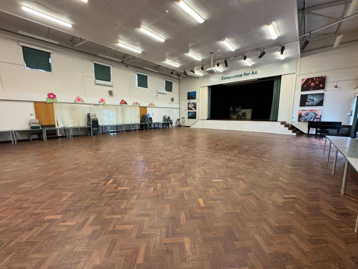 Large school event hall shoot space with parquet flooring, stage curtain backdrop, and high ceilings in Barnet N12 via Love Locations.
