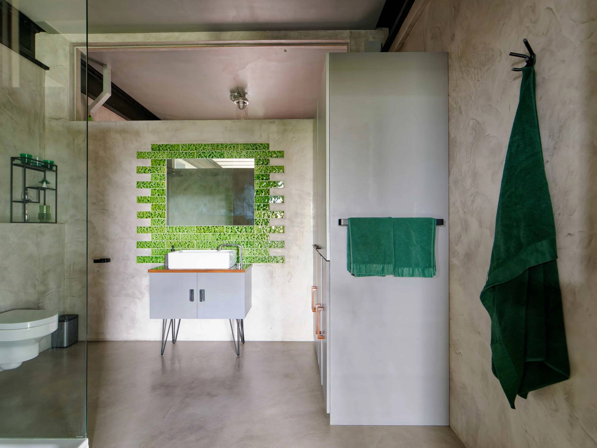 Minimalist micro-cement bathroom with white vanity unit and green tile splashback frame, ideal for skincare product ads, Love Locations E14.