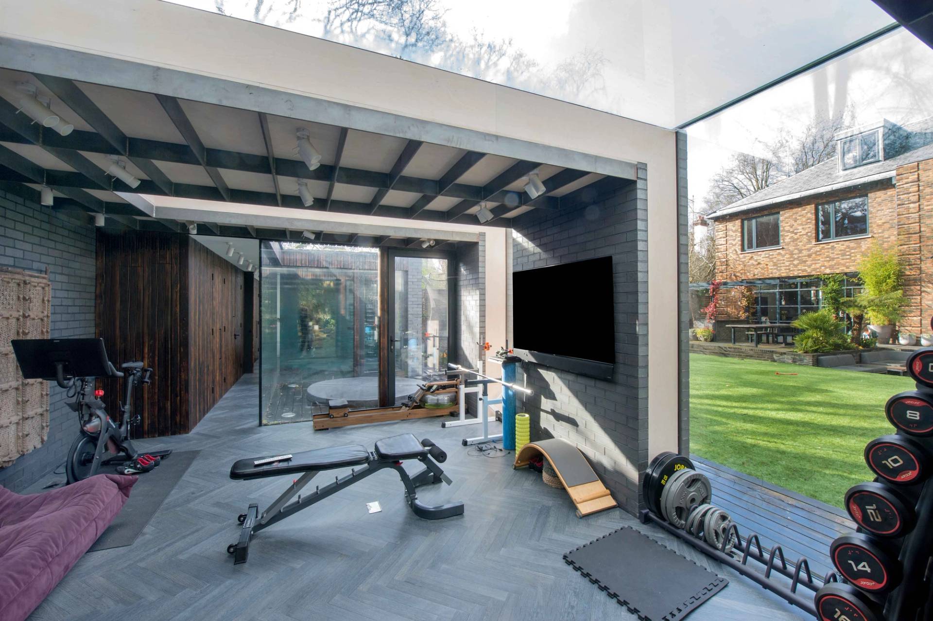 Modern home gym and fitness studio set inside a bright, glass-fronted garden pavilion with professional workout equipment, Love Locations NW3.