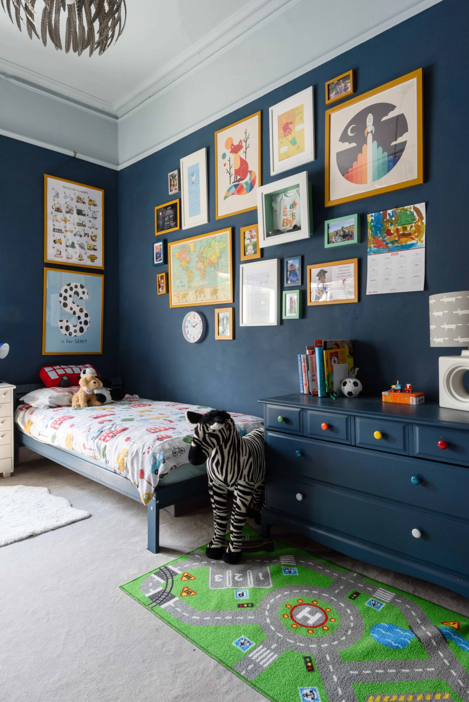 Dark navy blue kids bedroom featuring a gallery wall of framed art prints and dark blue chest of drawers, Love Locations TW11.