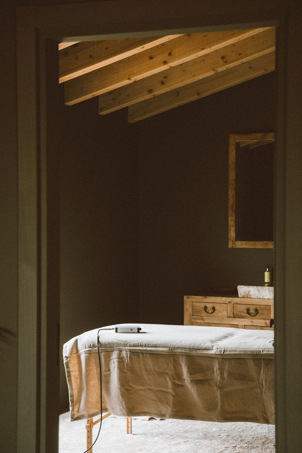 Spa massage room with a massage bed, dark green microcement walls, and wood ceiling beams, Love Locations 07630.