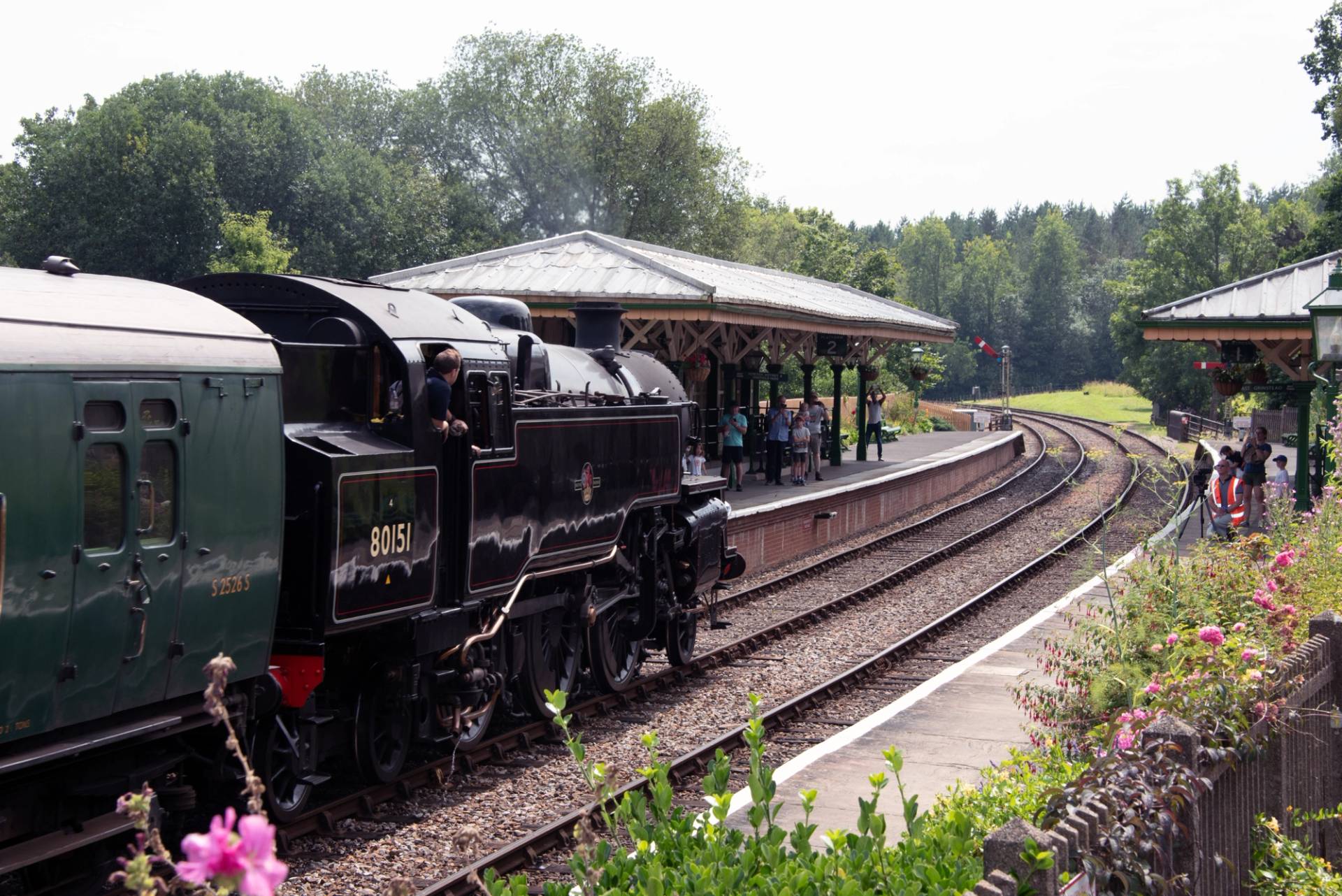 Black steam locomotive engine arriving at a rural covered station platform surrounded by trees, Love Locations TN22 3QL.