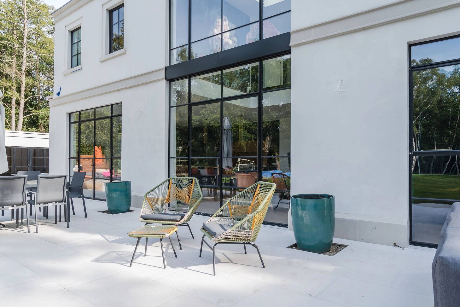 Modern mansion rear patio terrace with contemporary woven lounge chairs set outside floor-to-ceiling glass windows, Love Locations GU3.