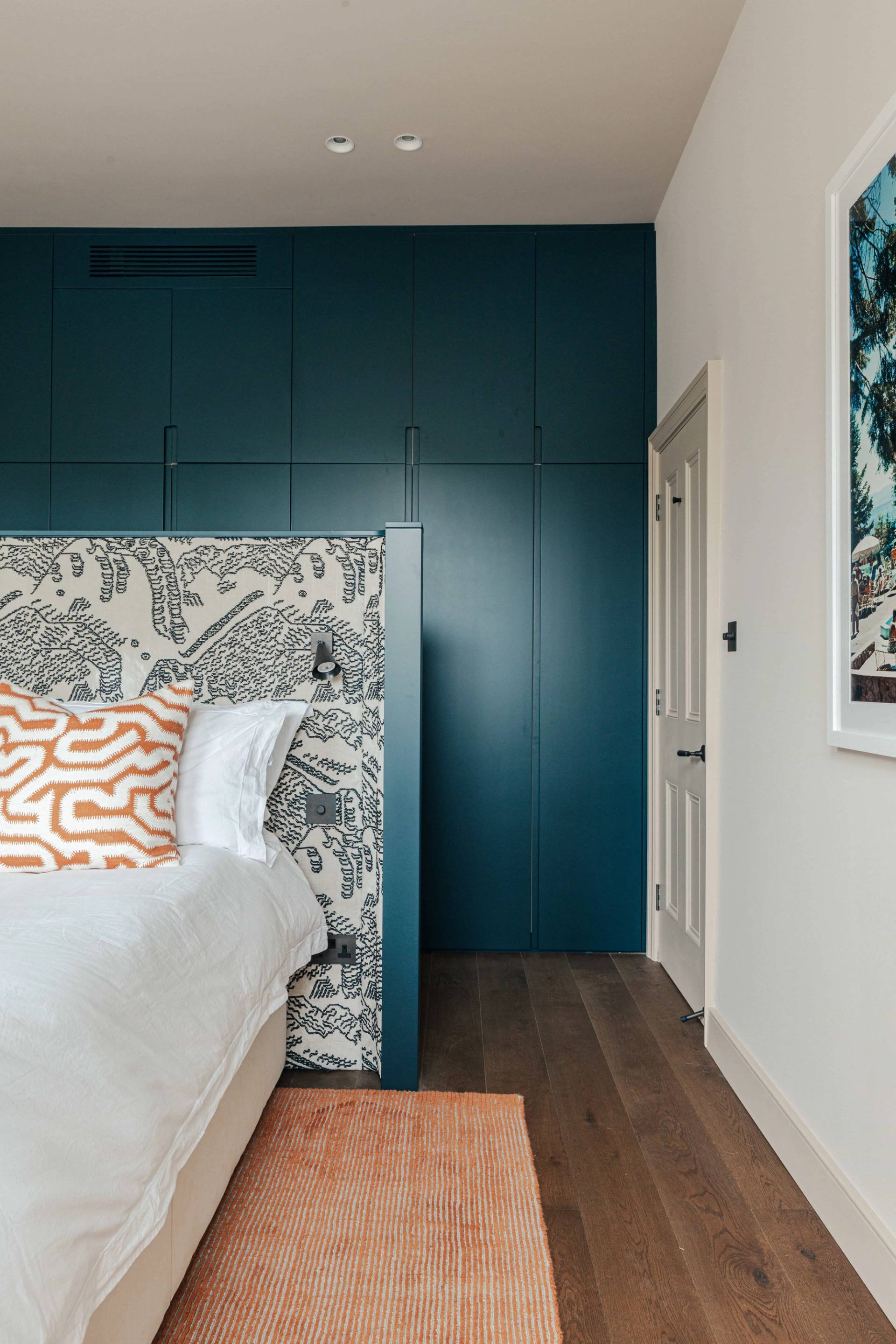 Bedroom view showing a patterned upholstered headboard set against deep blue wall storage, ideal for bedding lookbooks, Love Locations SW13.