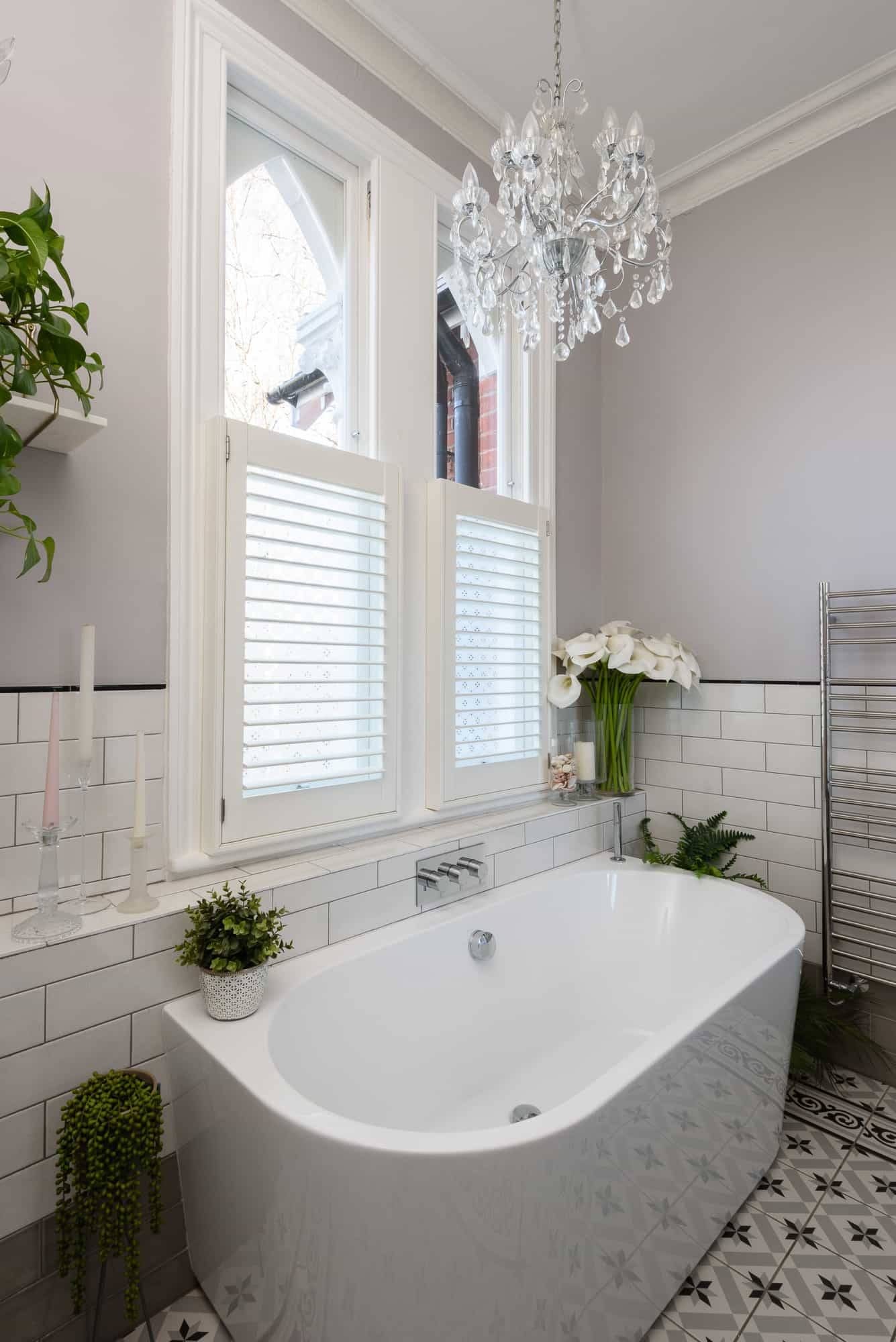Modern bathroom featuring a soaking tub, white subway tiles, crystal chandelier, and sash window shutters, Love Locations TW11.