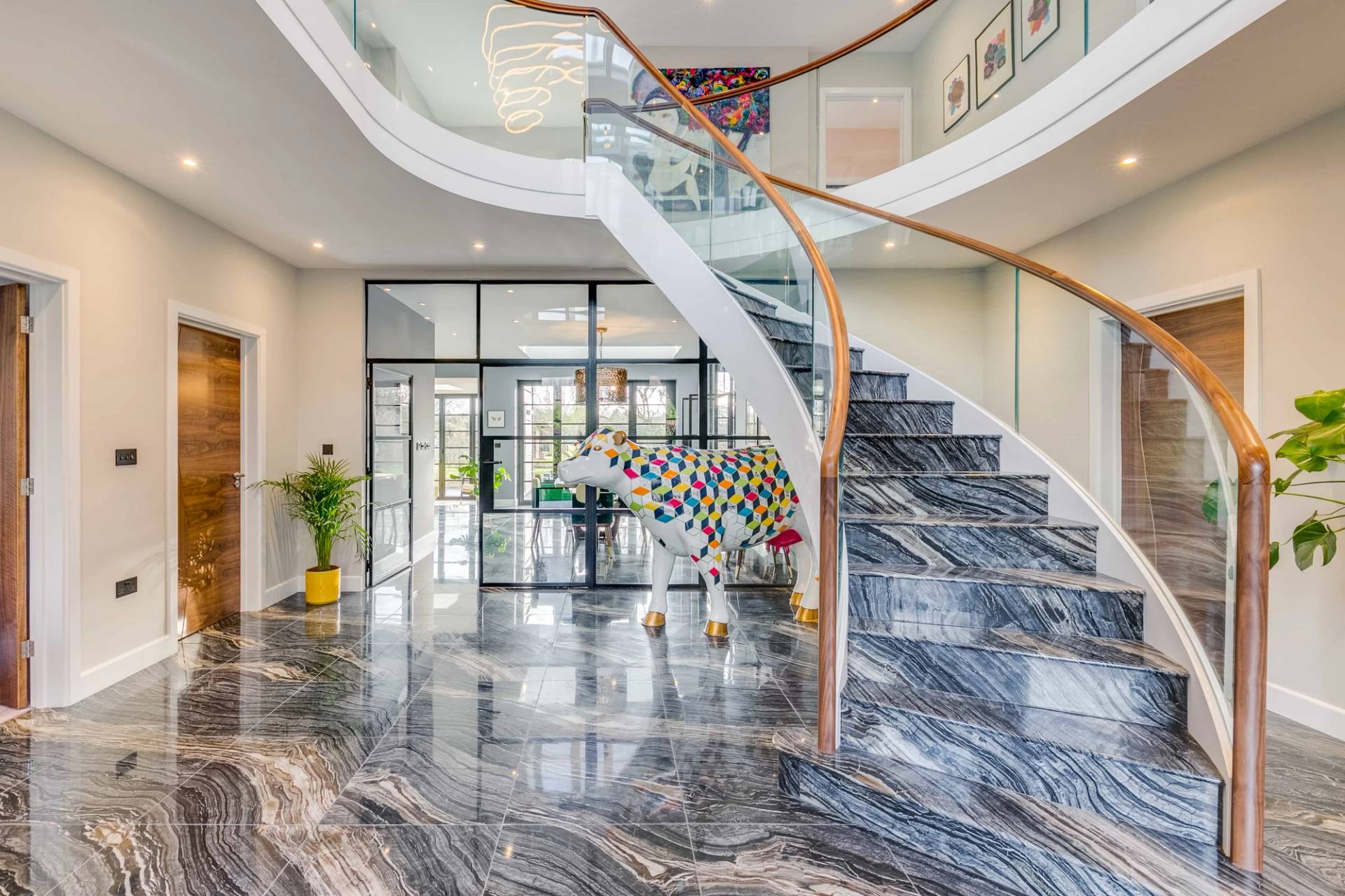 Curved grand staircase with glass balustrades set over polished dark marble floor tiles, Love Locations CB2.
