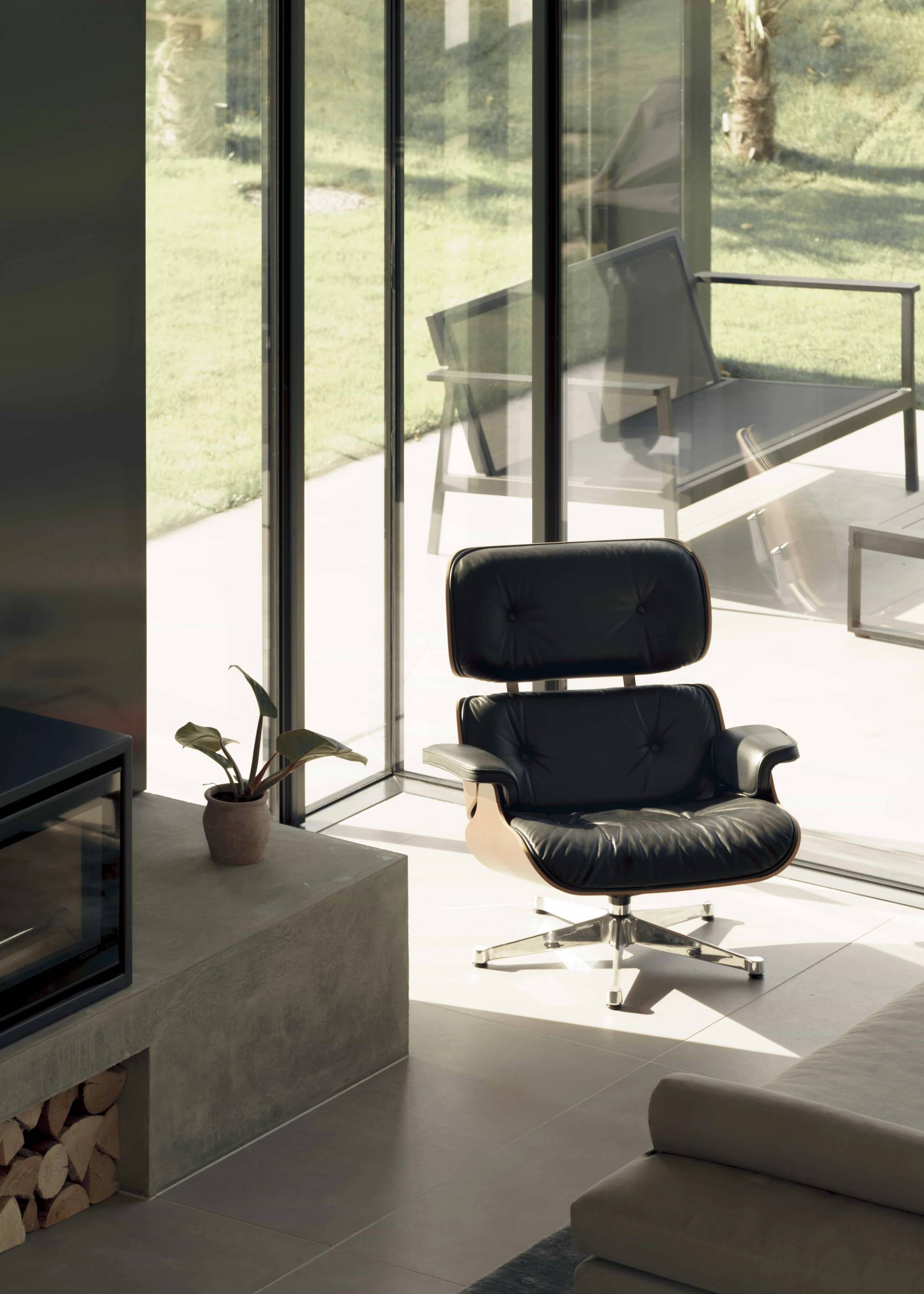 Sunlit architectural lounge corner featuring an Eames lounge chair and ottoman set beside full-height glass windows, Love Locations NR9.