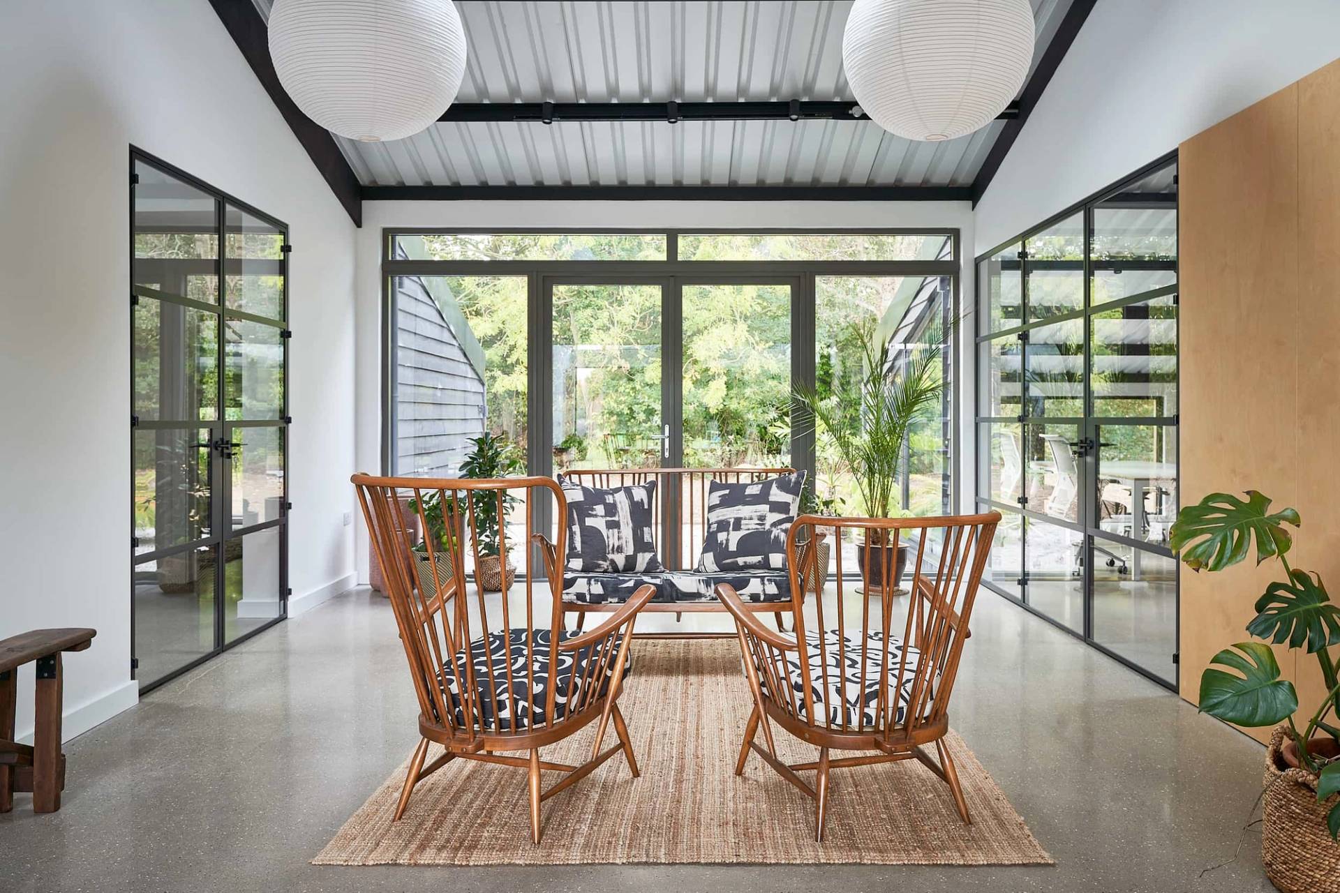 Crittall glass garden room with woven armchairs, jute rug, and corrugated metal roof ceilings, Love Locations IP30.