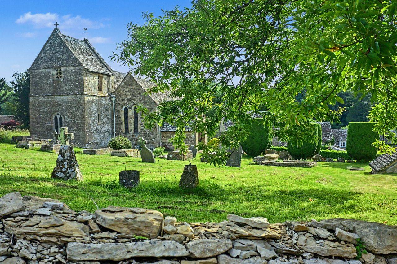 Churchyard and stone wall shoot location in Gloucestershire GL7 available from Love Locations, featuring lush green foliage, historical gravestones, and period architecture.