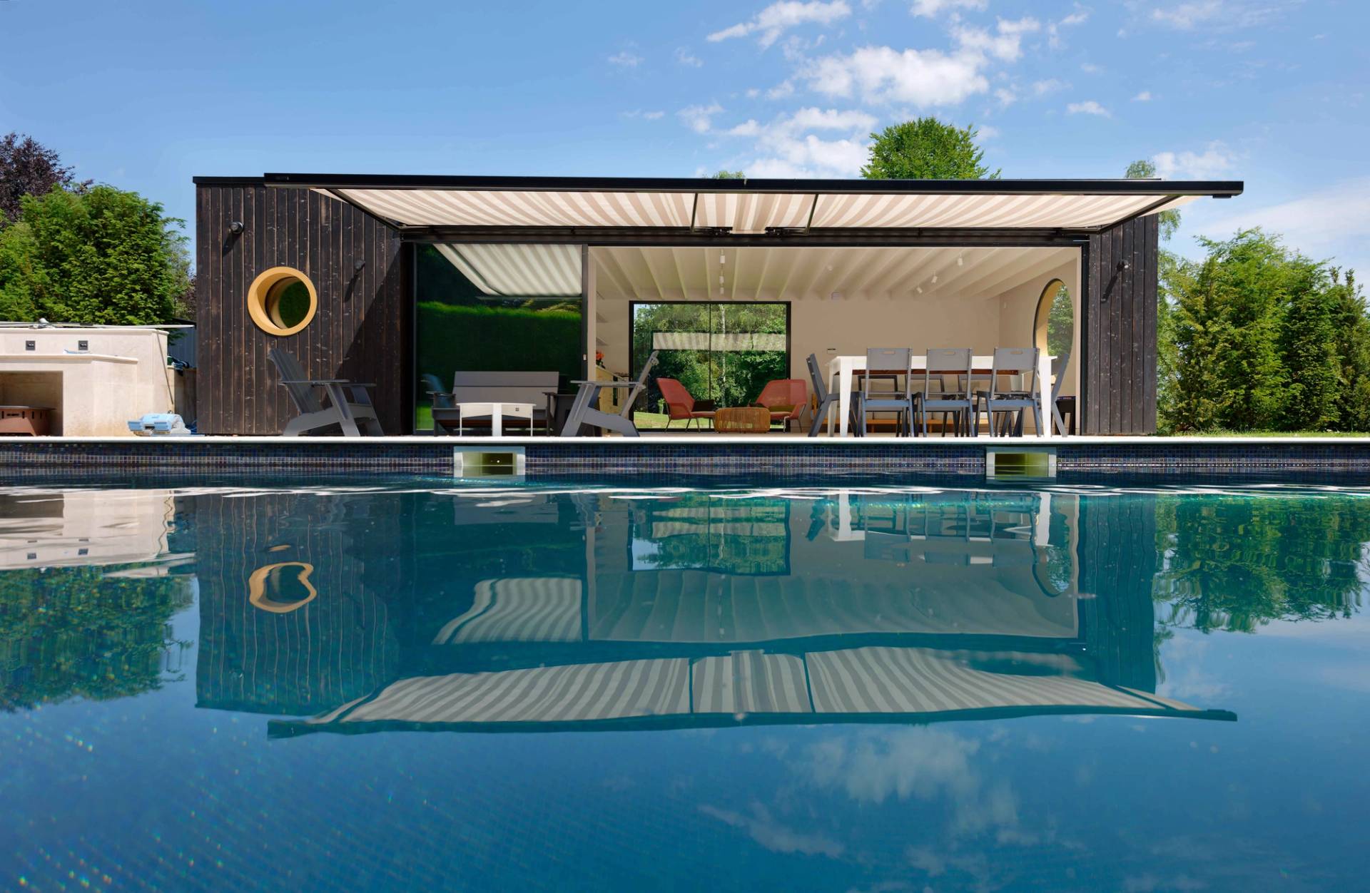 Luxury outdoor swimming pool set beside a modern black pool house with retractable roof pergola, Love Locations OX7.