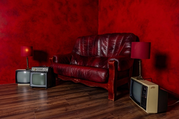 Retro red studio room in Tottenham, N15 with a red leather couch, vintage TV monitors, and dark wood flooring, Love Locations.