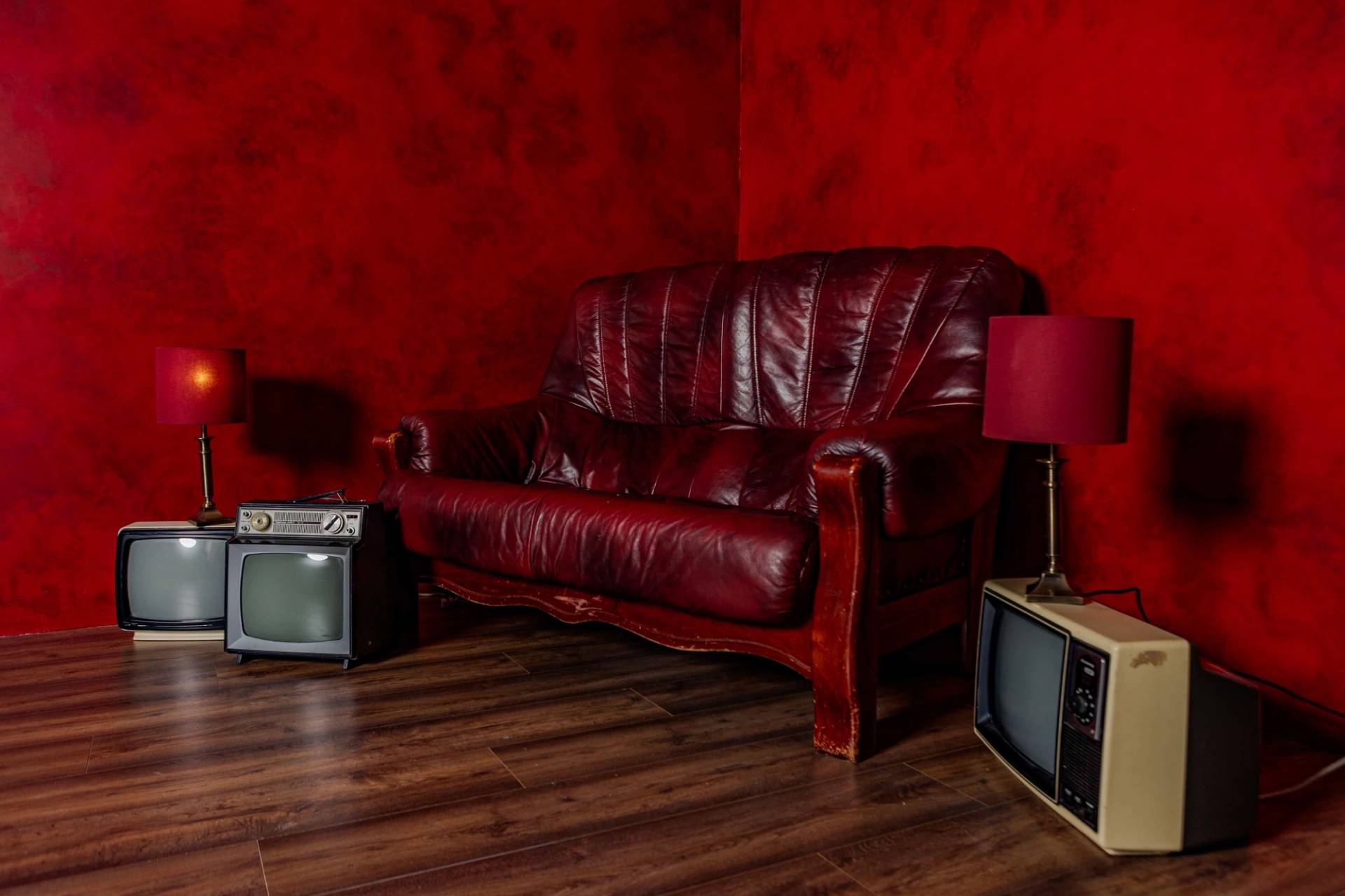 Retro red studio room in Tottenham, N15 with a red leather couch, vintage TV monitors, and dark wood flooring, Love Locations.