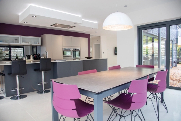 Bright modern dining area attached to a luxury kitchen featuring vibrant purple chairs, suitable for family sit-com TV scenes, Love Locations GU5.
