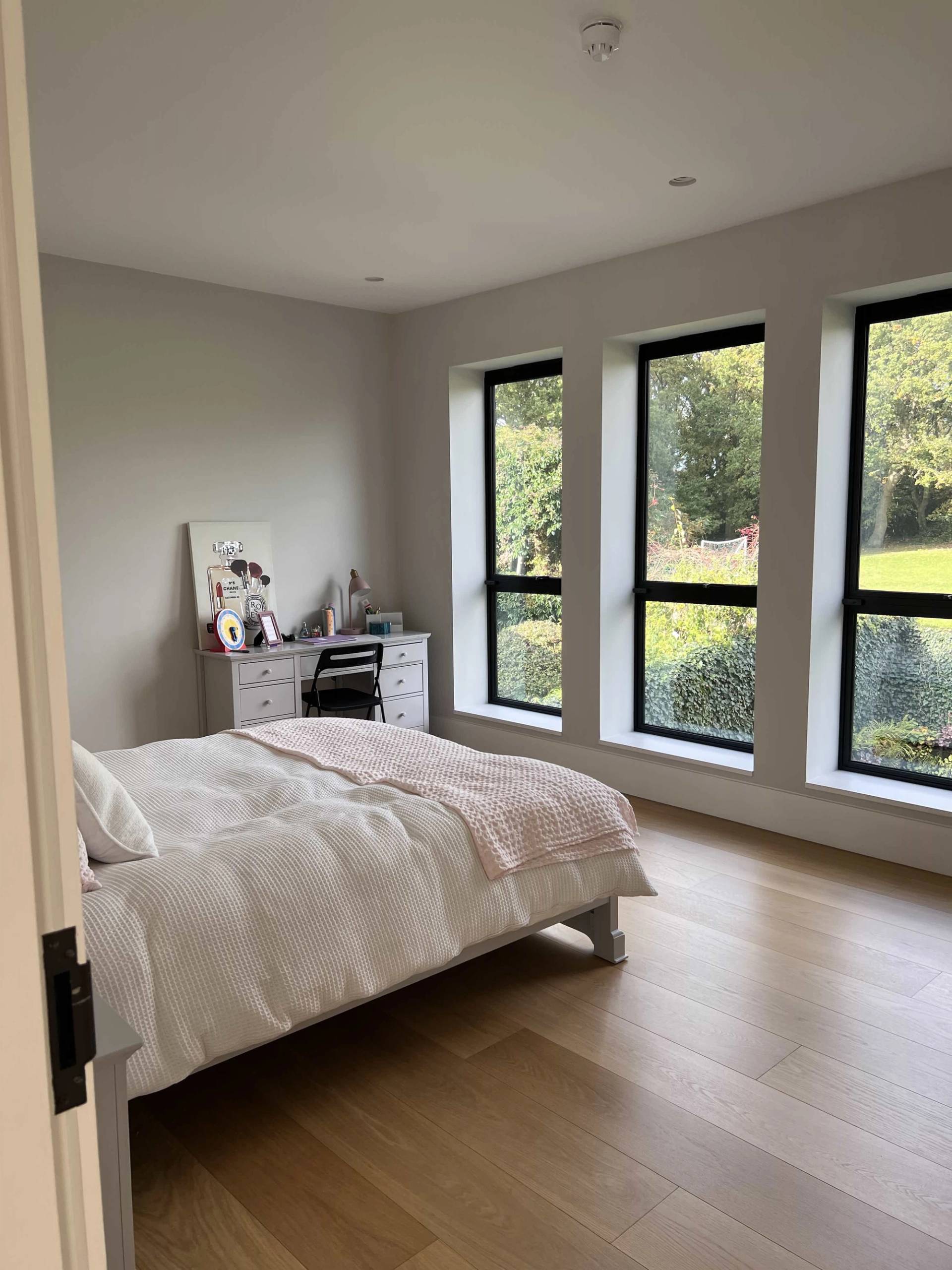 Light-filled guest bedroom featuring three tall black-framed windows, light wood floors, and neutral styling, ideal for home decor lookbooks, Love Locations N3.