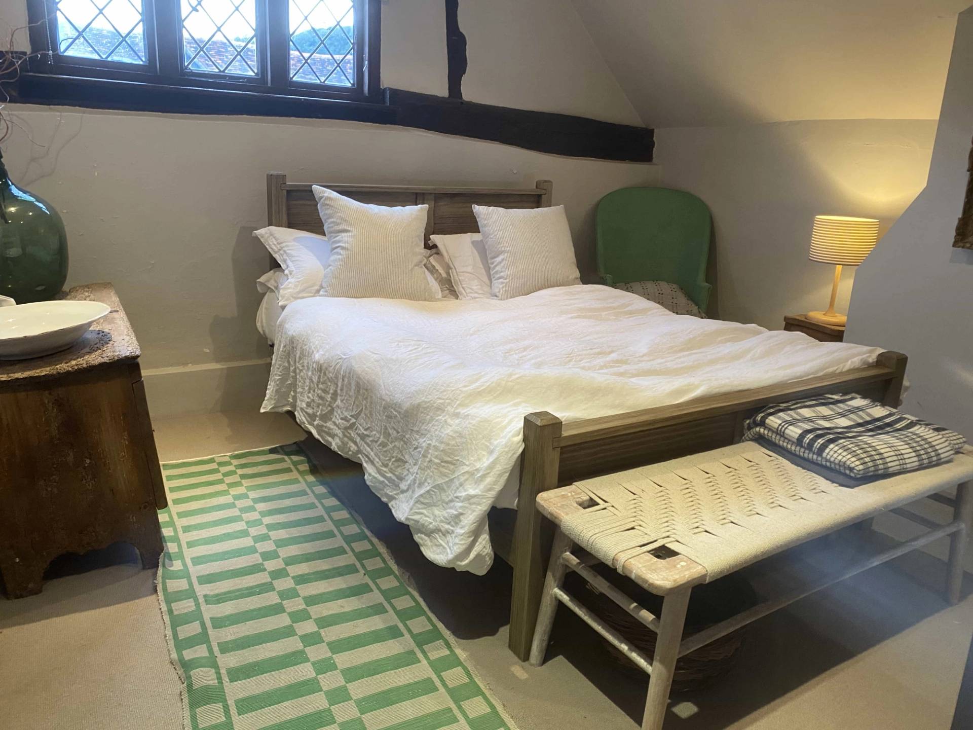 Charming Tudor cottage double bedroom shoot location featuring white linens, a wooden bed frame, and traditional leaded windows, Love Locations RG9 6QD.