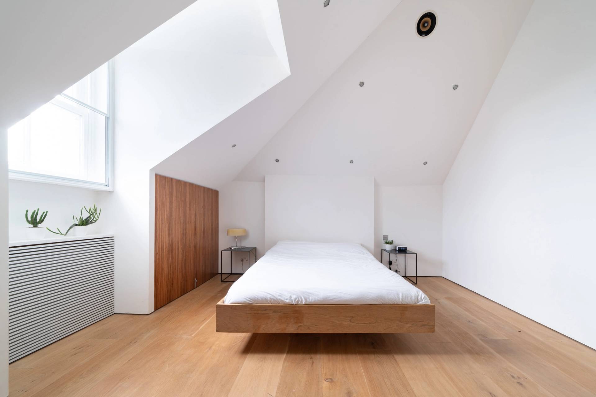 Loft bedroom suite featuring sloped ceiling skylights, built-in timber storage, and white linen bedding, Love Locations SW6.